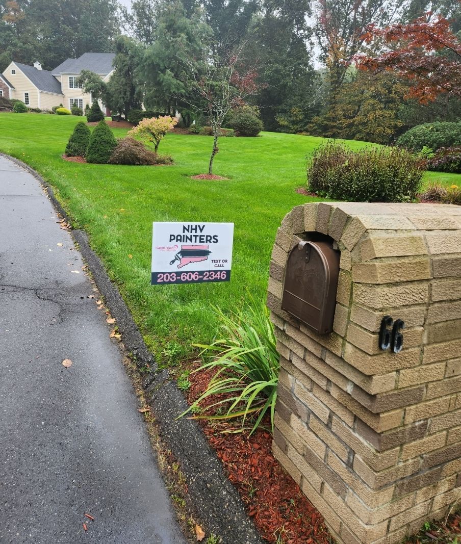Lush green lawn with a brick mailbox and a sign for a landscape service; a house is in the background.