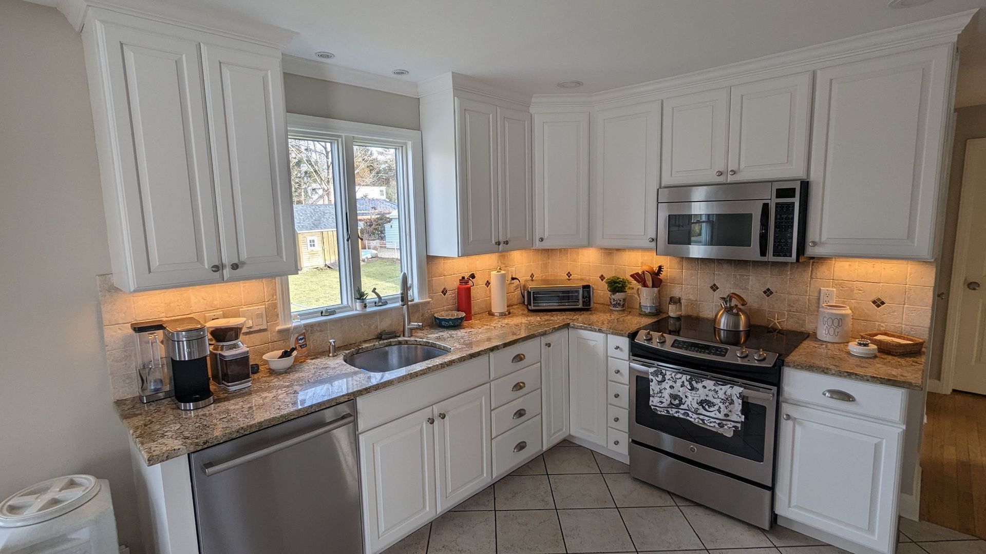 A kitchen with white cabinets , stainless steel appliances , granite counter tops and a window.
