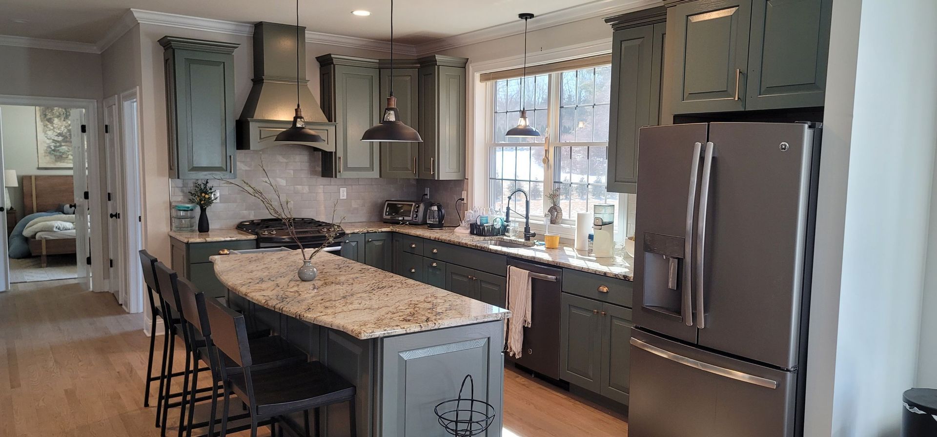 A kitchen with green cabinets , granite counter tops , stainless steel appliances and a large island.