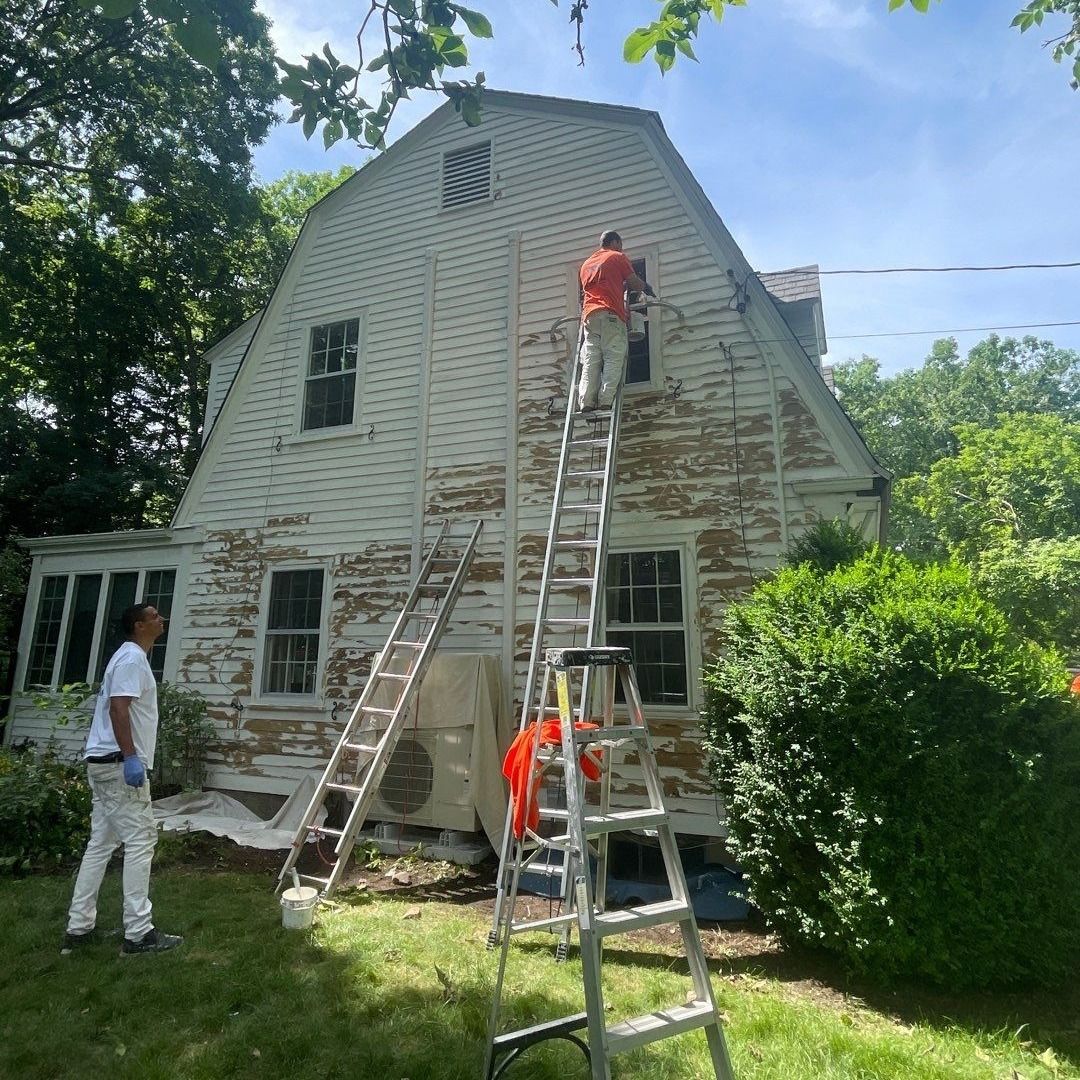 A man on a ladder is painting the side of a house