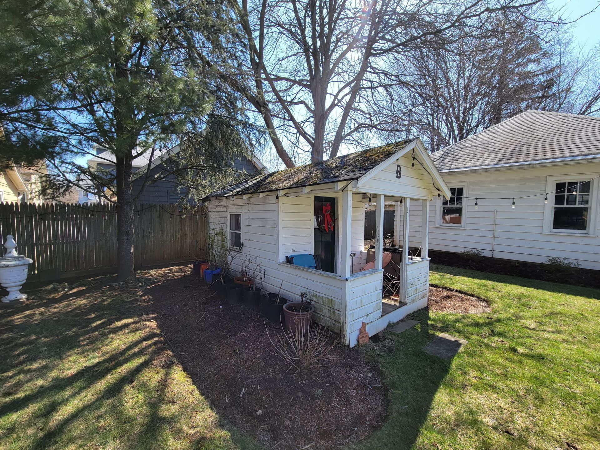 A small white house with a porch in the backyard of a house.