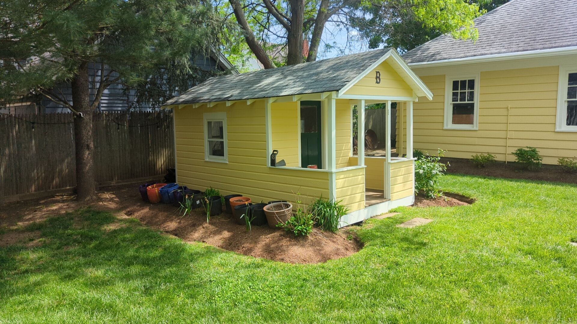 A small yellow playhouse is sitting in the grass in front of a yellow house.
