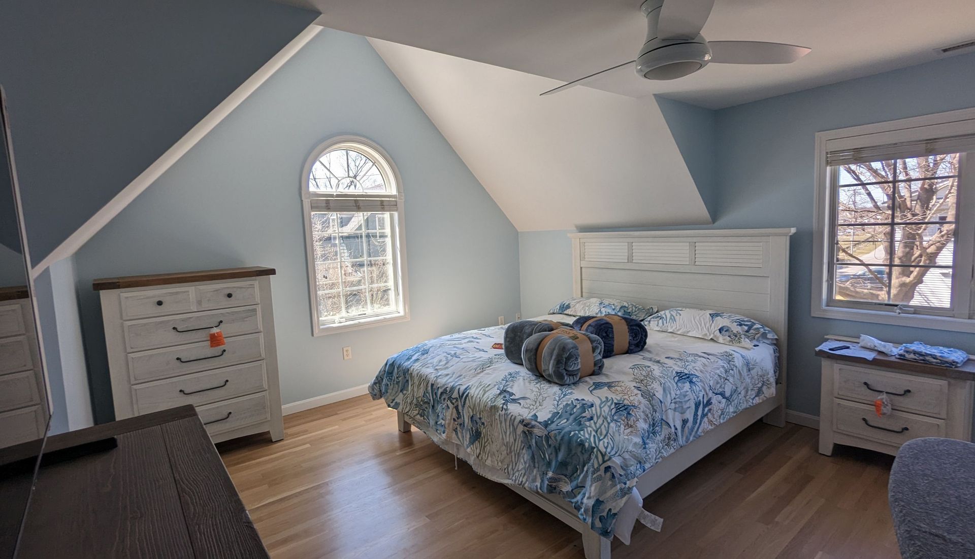 Bedroom with blue walls, white bed, and two dressers. A window allows natural light.
