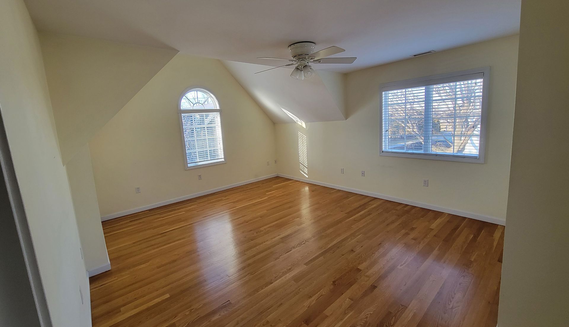 Empty room with hardwood floors, two windows, and a ceiling fan.