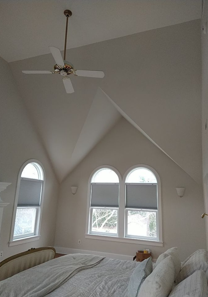 A bedroom with a bed , ceiling fan , and arched windows.