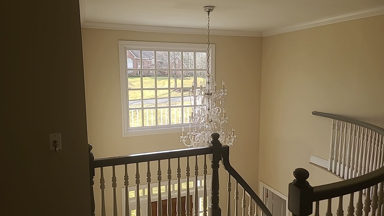 A staircase with a chandelier hanging from the ceiling and a window.