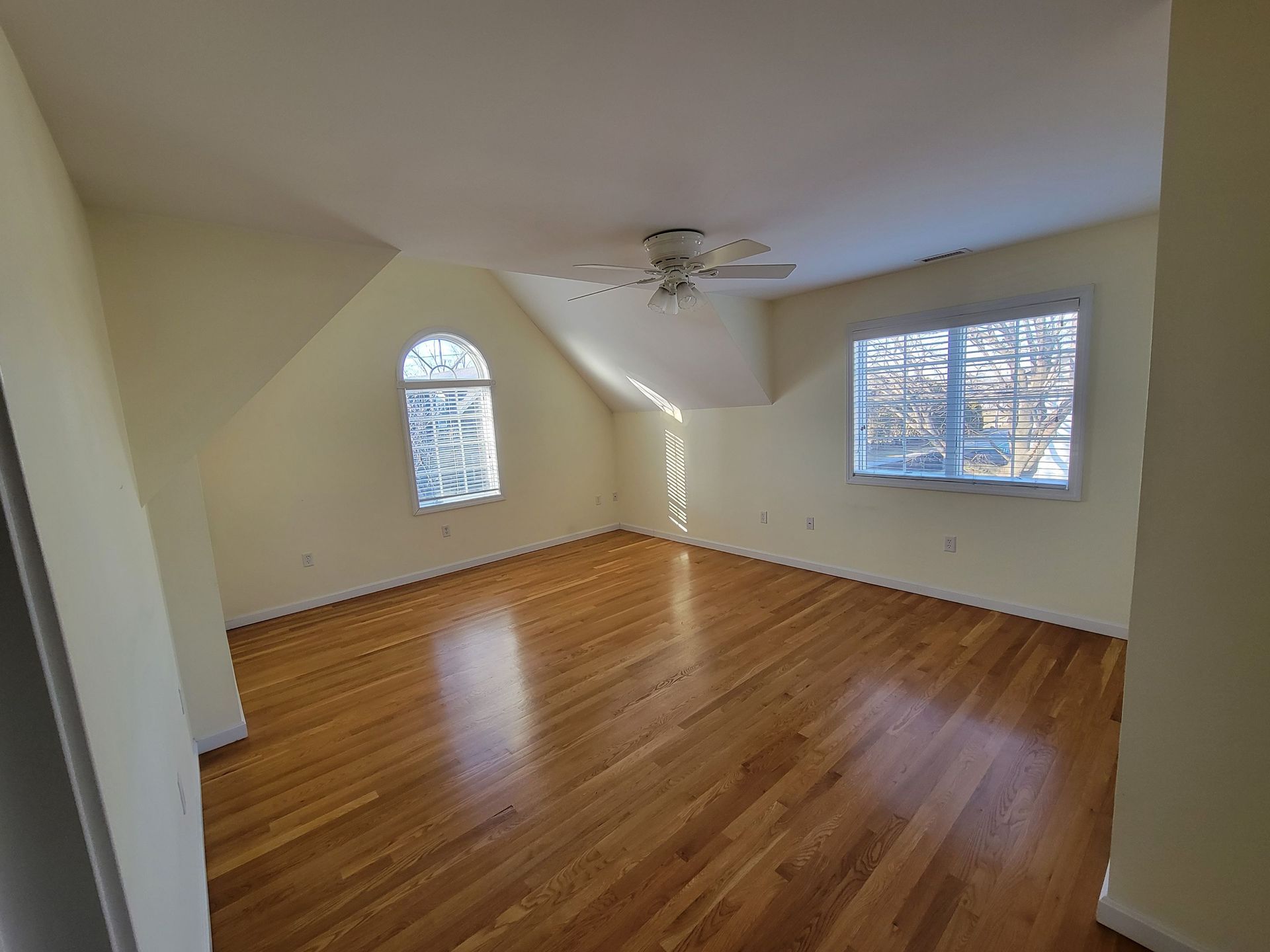 A large empty room with hardwood floors and a ceiling fan.