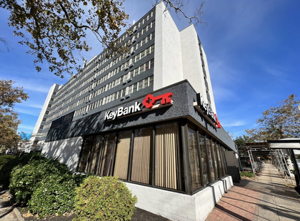 KeyBank building with red signage. Tall, white building with a modern glass-walled base, and a blue sky in the background.