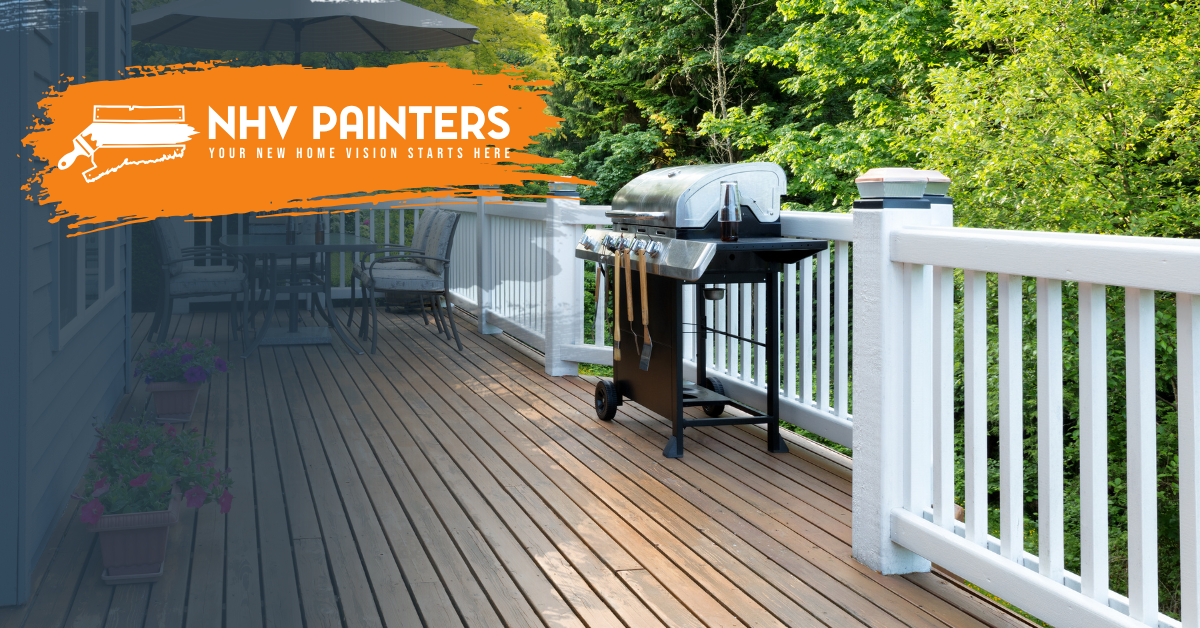 Deck with wooden boards, white railing, grill, and orange NHV Painters banner on a tree-lined patio