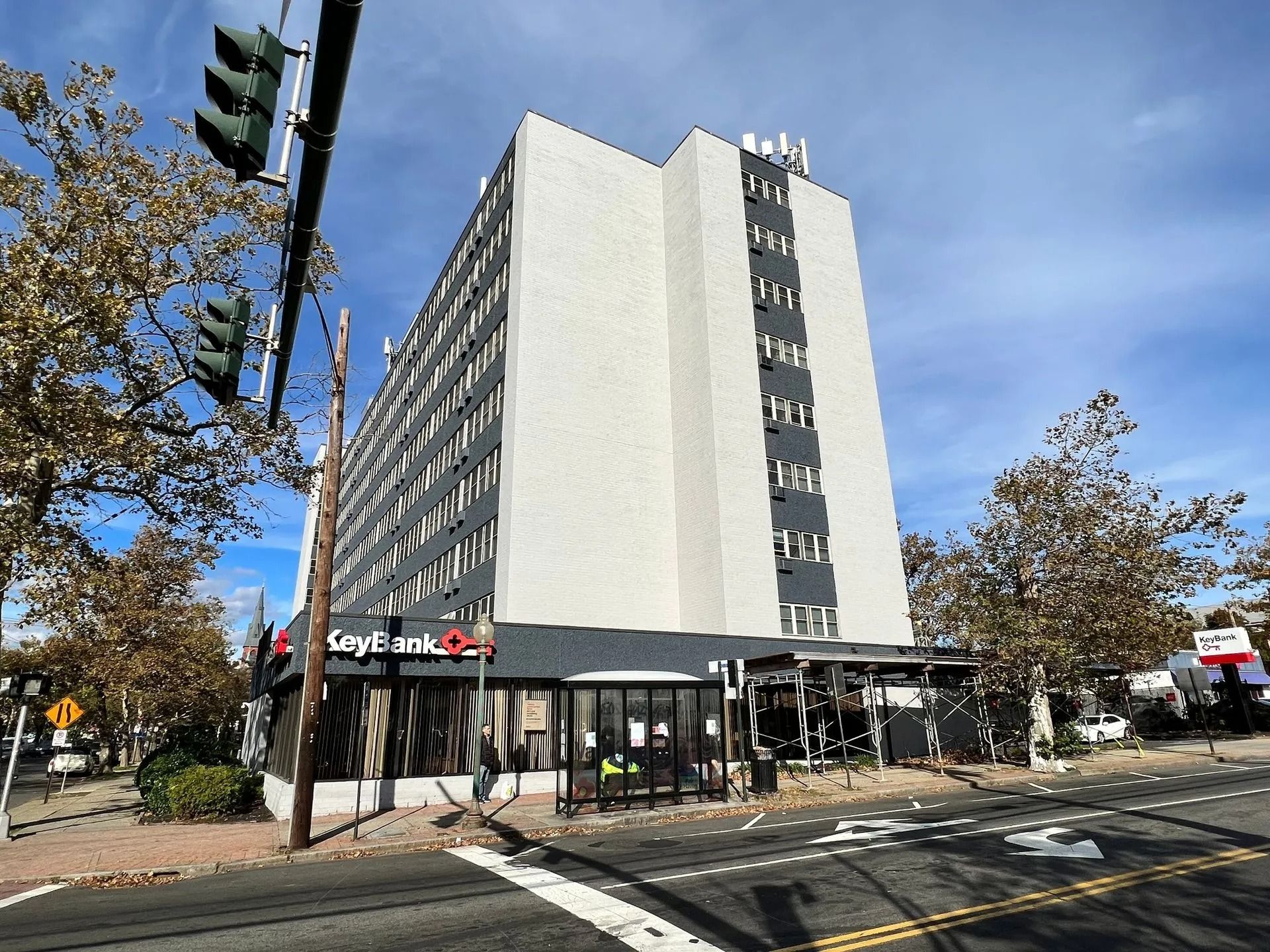 A tall, light-colored building with dark gray trim. A bank is on the first floor with a covered outdoor seating area.