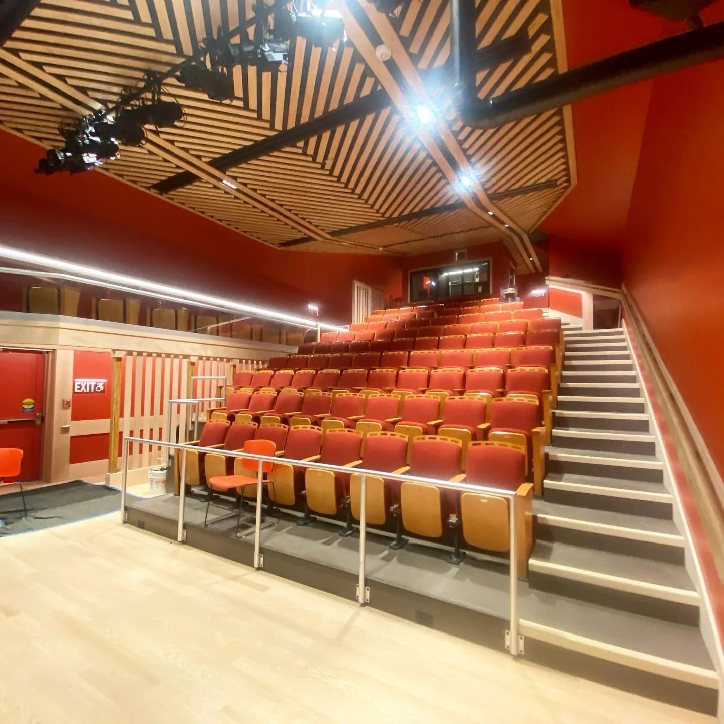 Interior of a small theater with red seats, walls, and a wood-paneled ceiling. A staircase leads to the seating area.