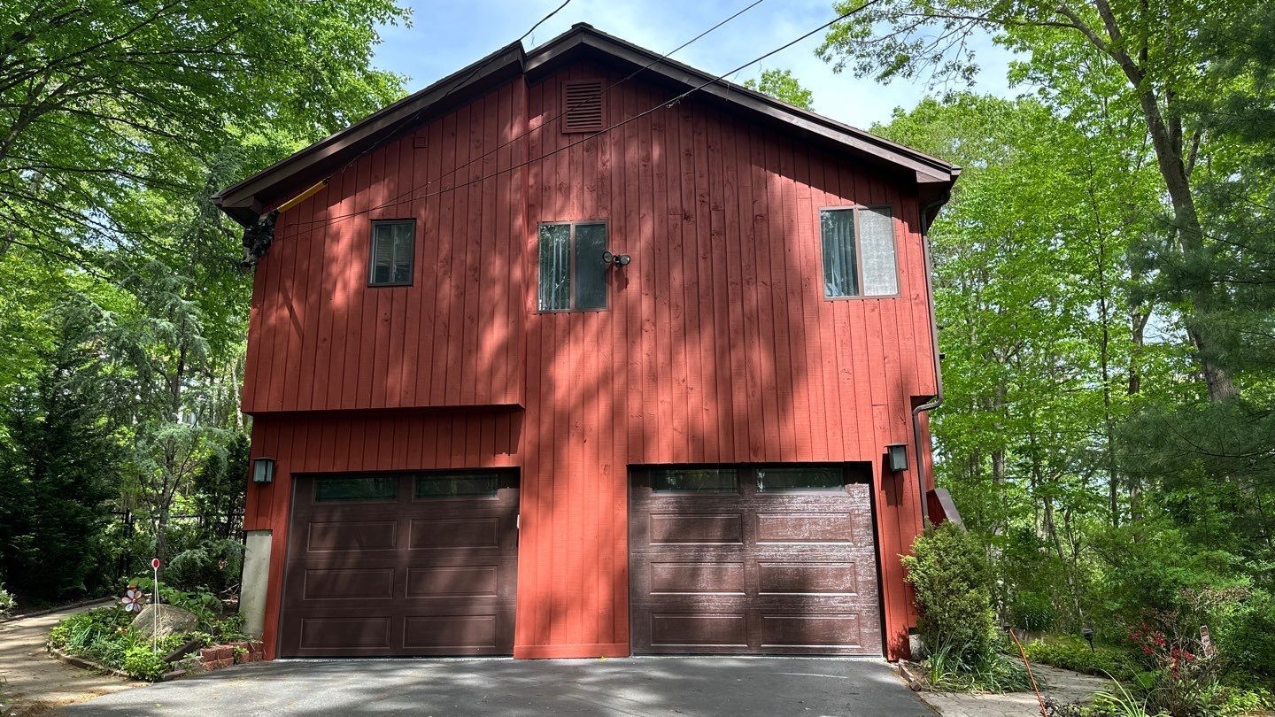 A red barn with two garage doors is surrounded by trees.