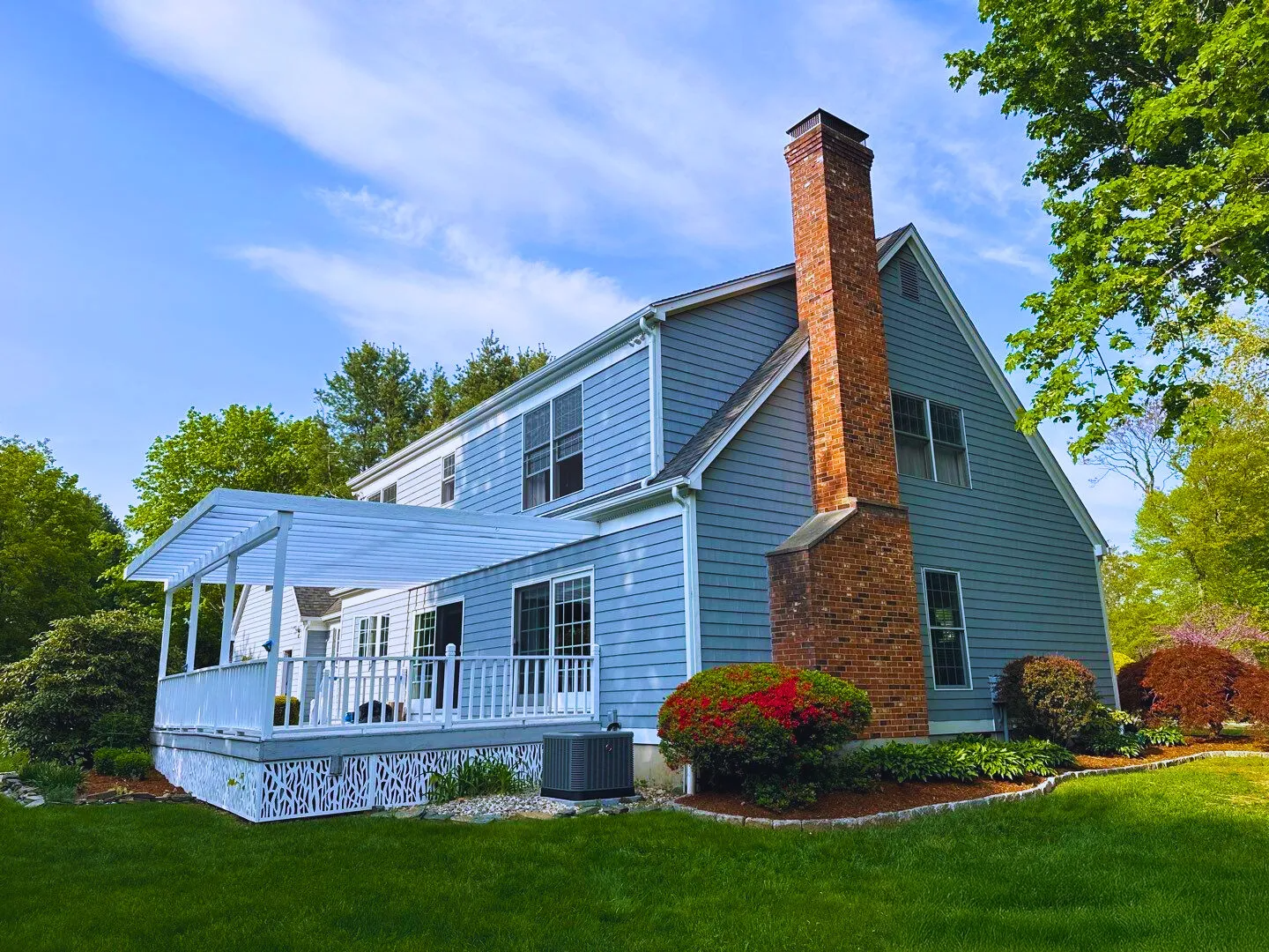 Blue house with white porch and red brick chimney on a grassy lawn under a blue sky.