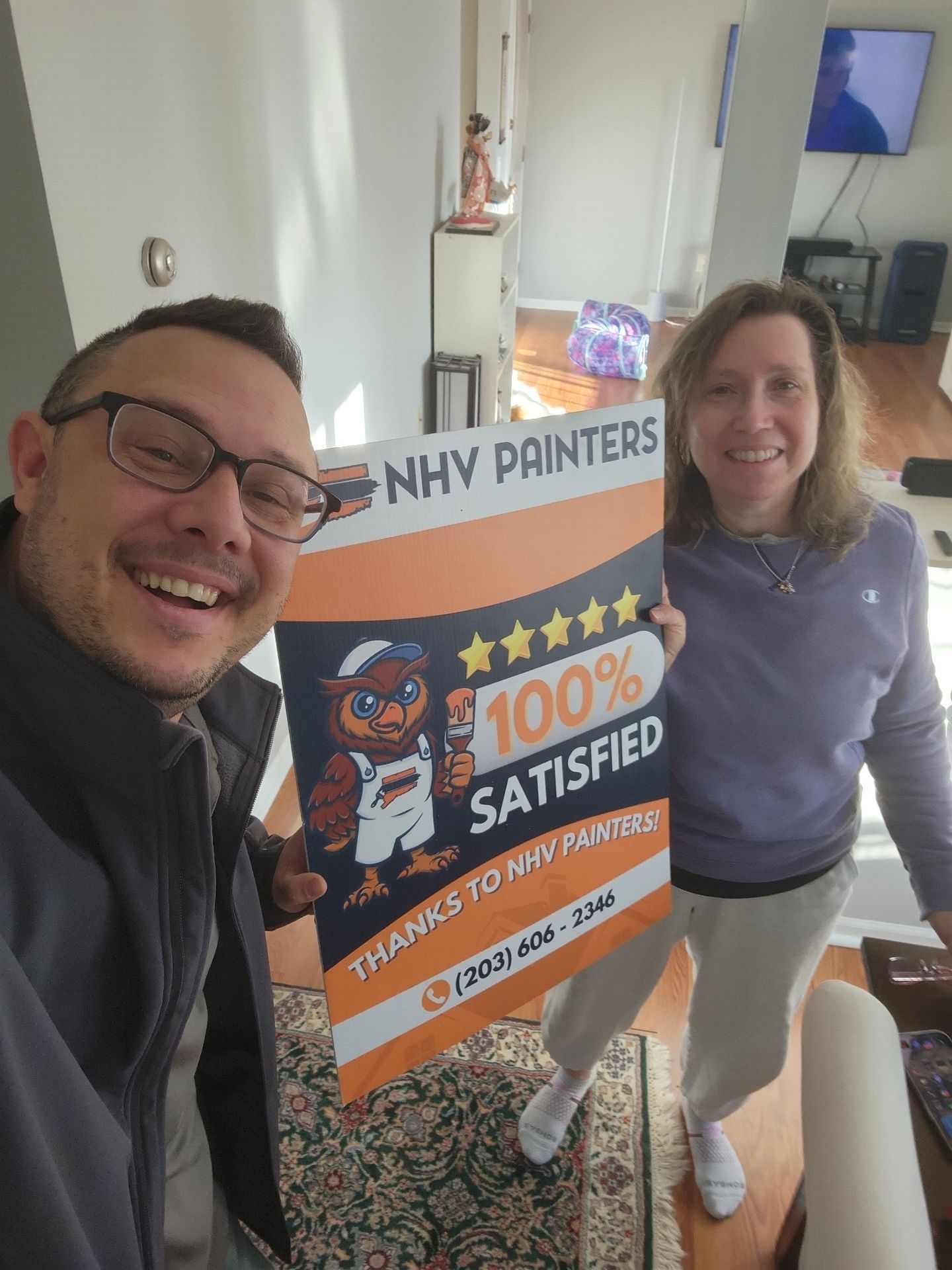 Two people smiling, holding a sign for NHY Painters, stating 
