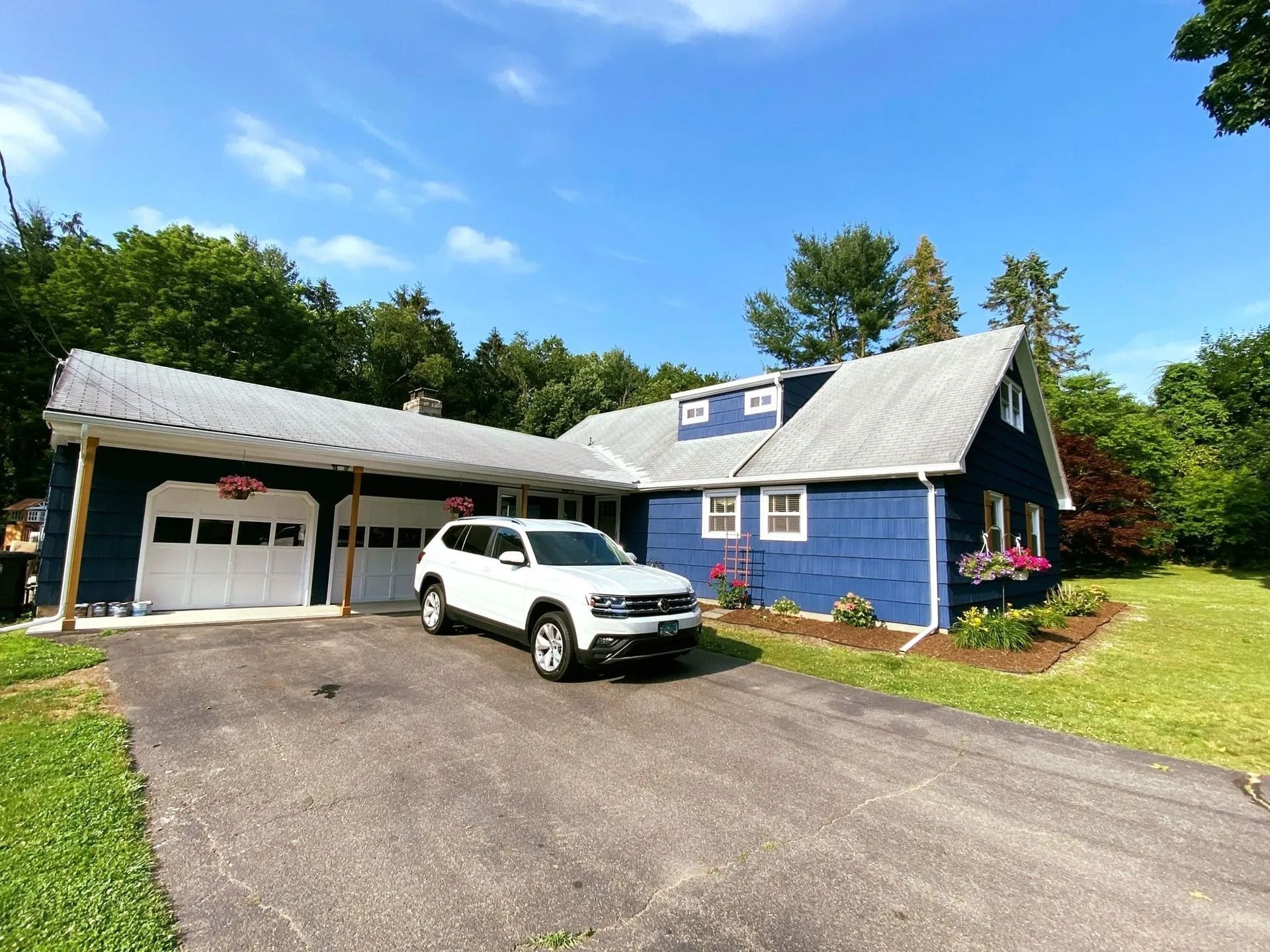 Blue house with attached garage and carport, white SUV parked in the driveway. Sunny day.