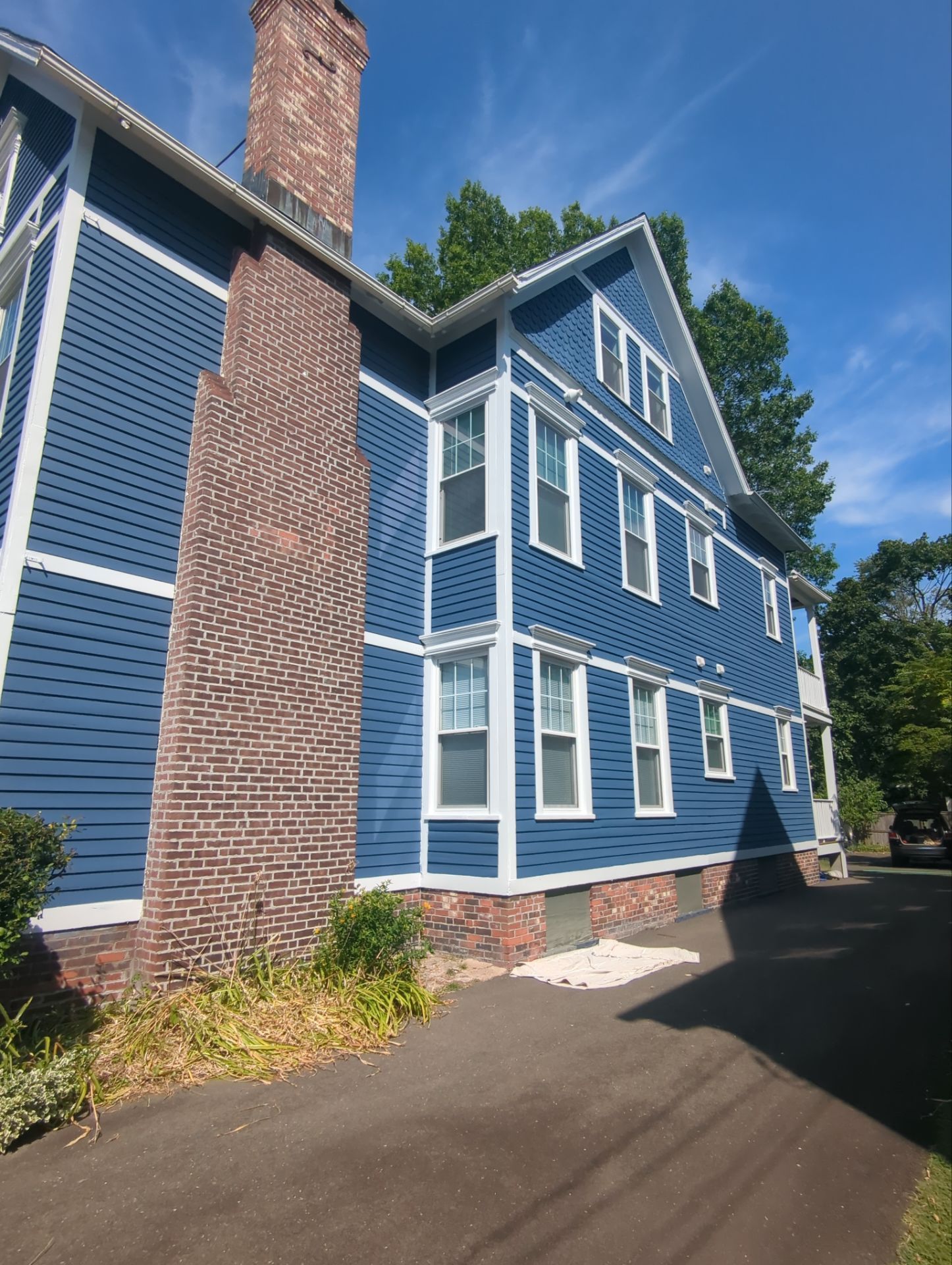 Blue multi-story building with white trim, a brick chimney, and a driveway.