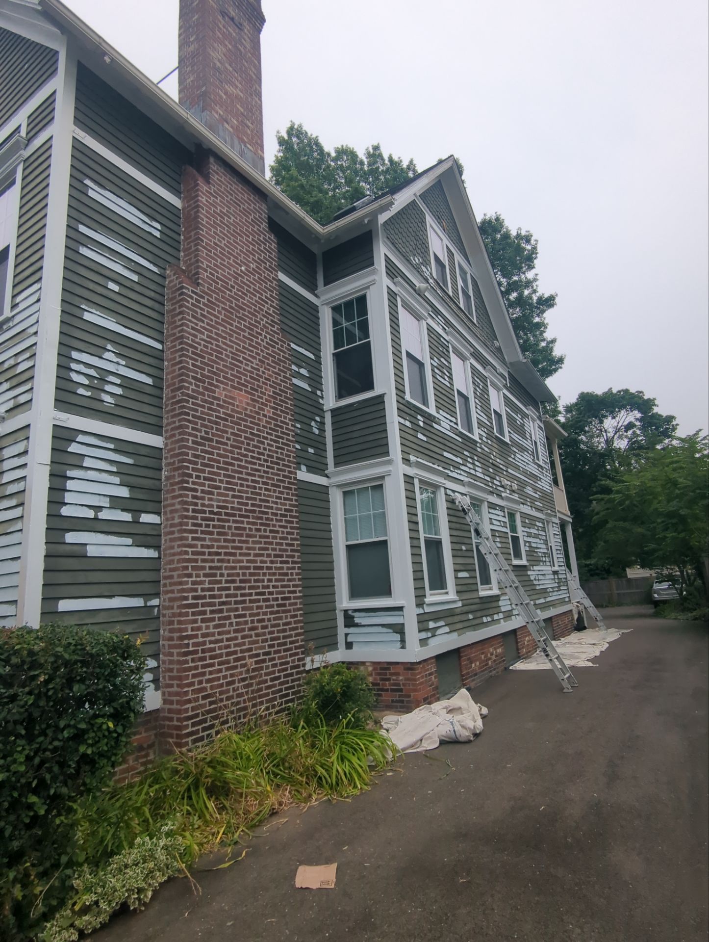 Multi-story building with peeling green paint, red brick chimney, and ladder leaning against the side.