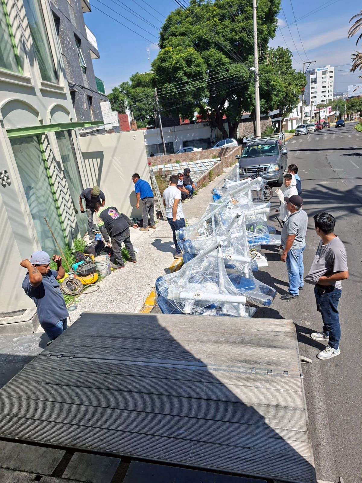 Obreros descargando estructuras metálicas de un camión en una calle de la ciudad. Varias personas se encuentran cerca.