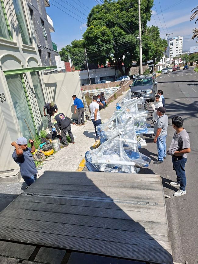 Trabajadores descargando equipo de un camión en una calle de la ciudad. Día soleado.
