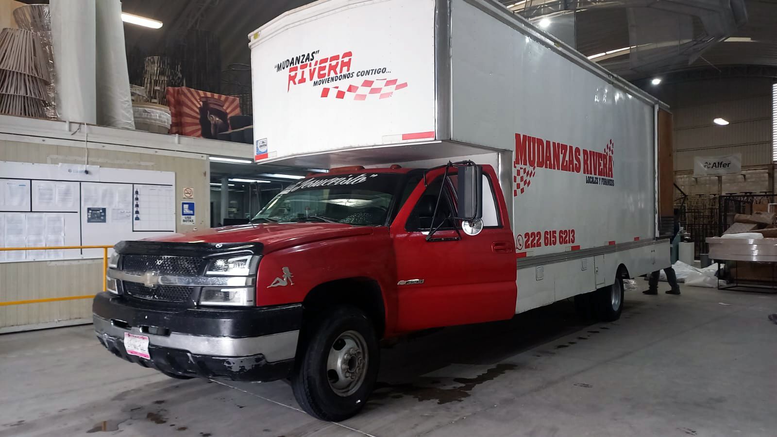 Camión de reparto rojo y blanco dentro de un almacén. La puerta del conductor está abierta.
