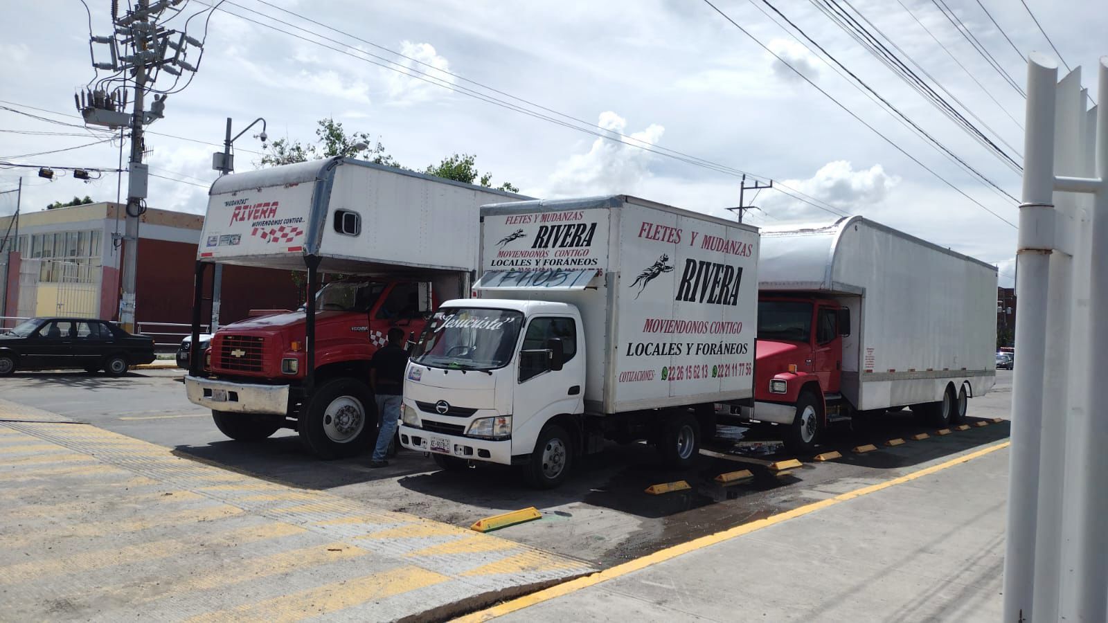 Tres camiones de mudanza estacionados afuera. Uno es rojo y grande, y dos son blancos.