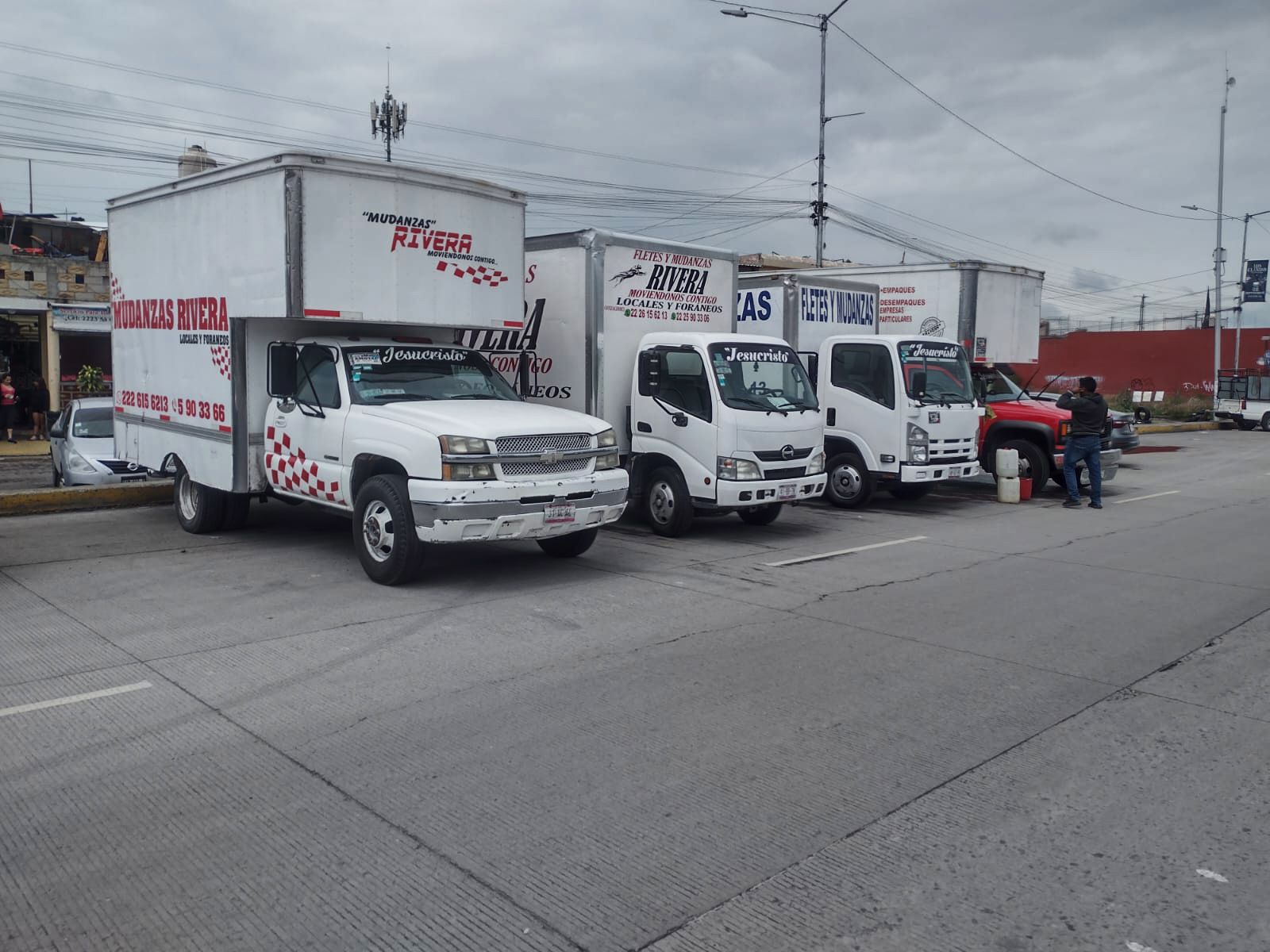 Cuatro camiones de reparto blancos estacionados en una calle gris bajo un cielo nublado.