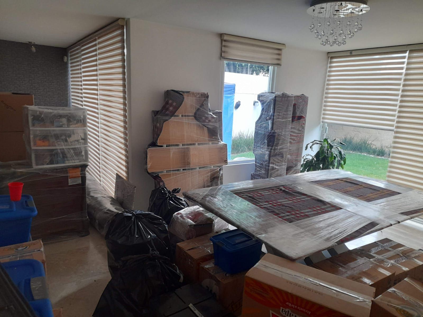 Una habitación llena de cajas empaquetadas y muebles envueltos en plástico, listos para mudarse.