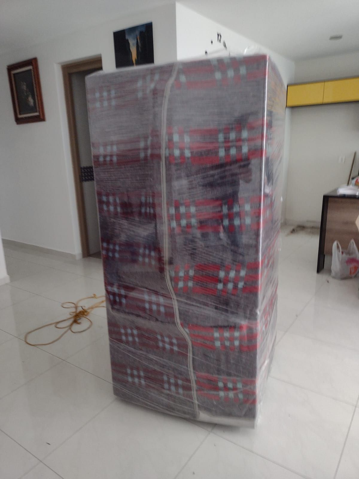 Cajas envueltas y apiladas en una habitación con una puerta, una pintura y una lámpara de pared amarilla.