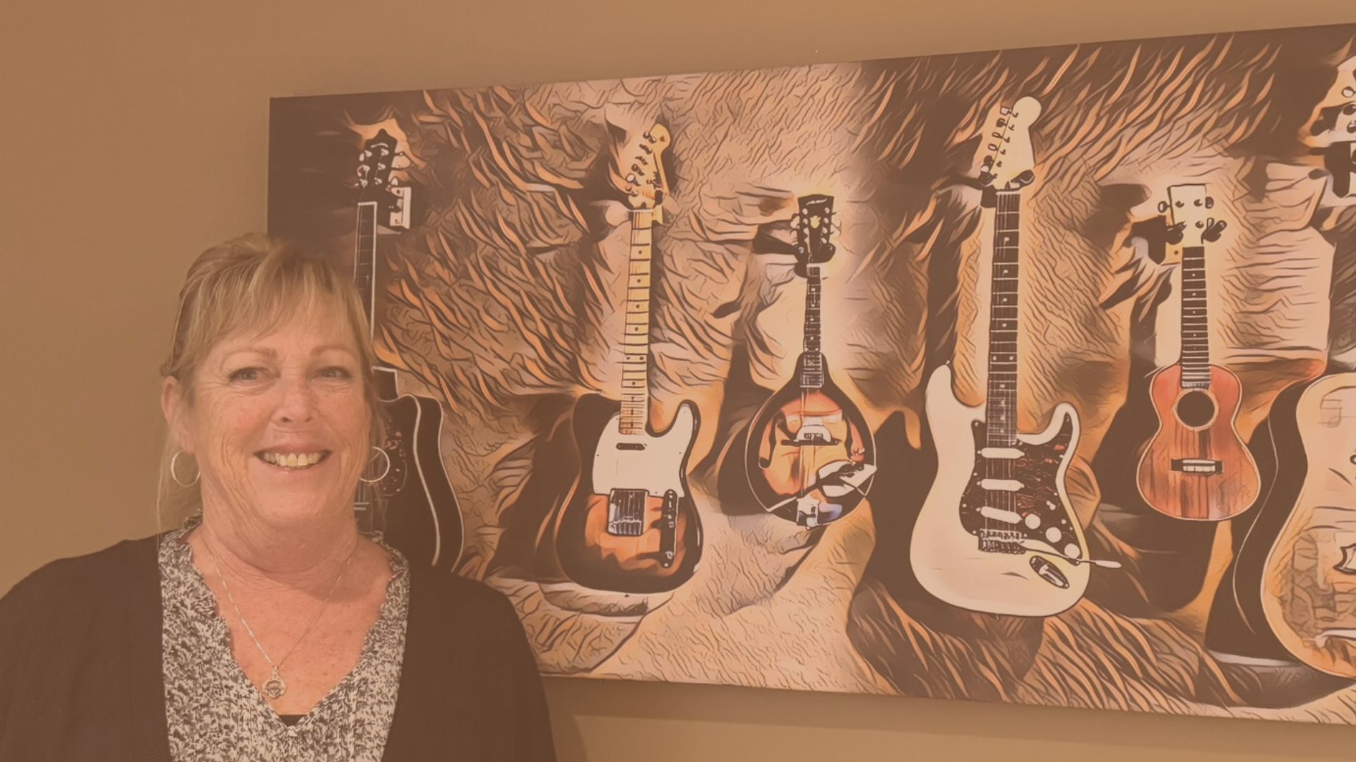 smiling blonde woman in front of large artwork featuring a variety of guitars