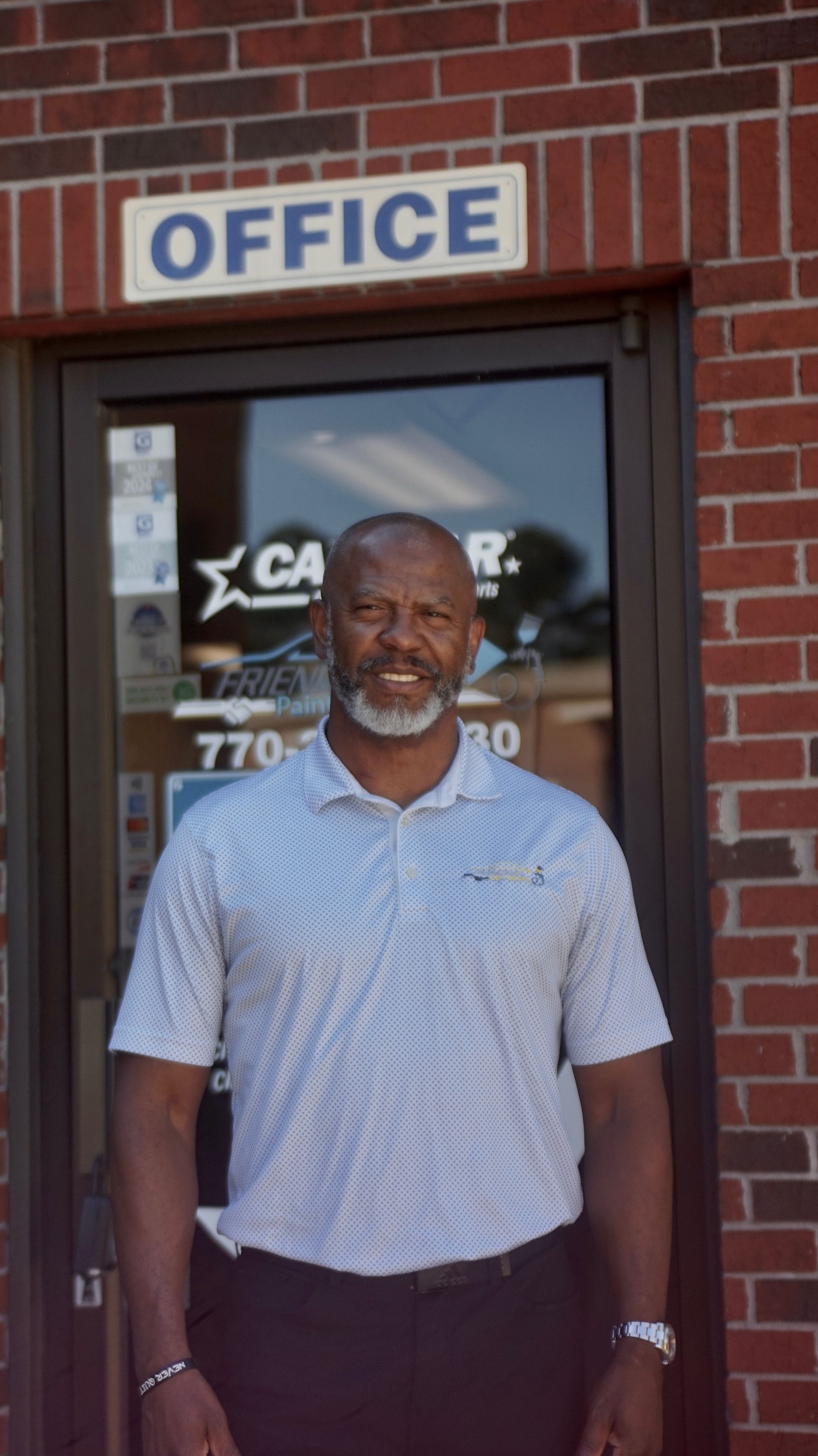 Man standing in front of an office entrance with a brick wall and “OFFICE” sign above the door