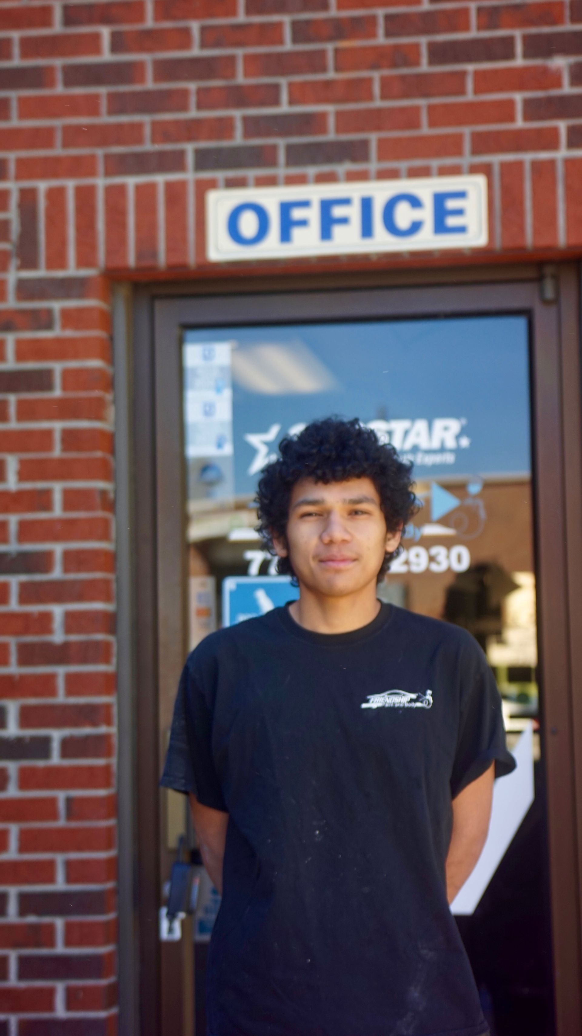 Person standing in an office doorway beneath an “OFFICE” sign, wearing a black T-shirt.