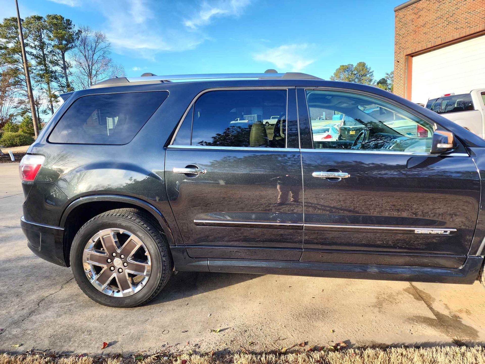 Black SUV parked in a driveway beside a garage, viewed from the side under a sunny sky