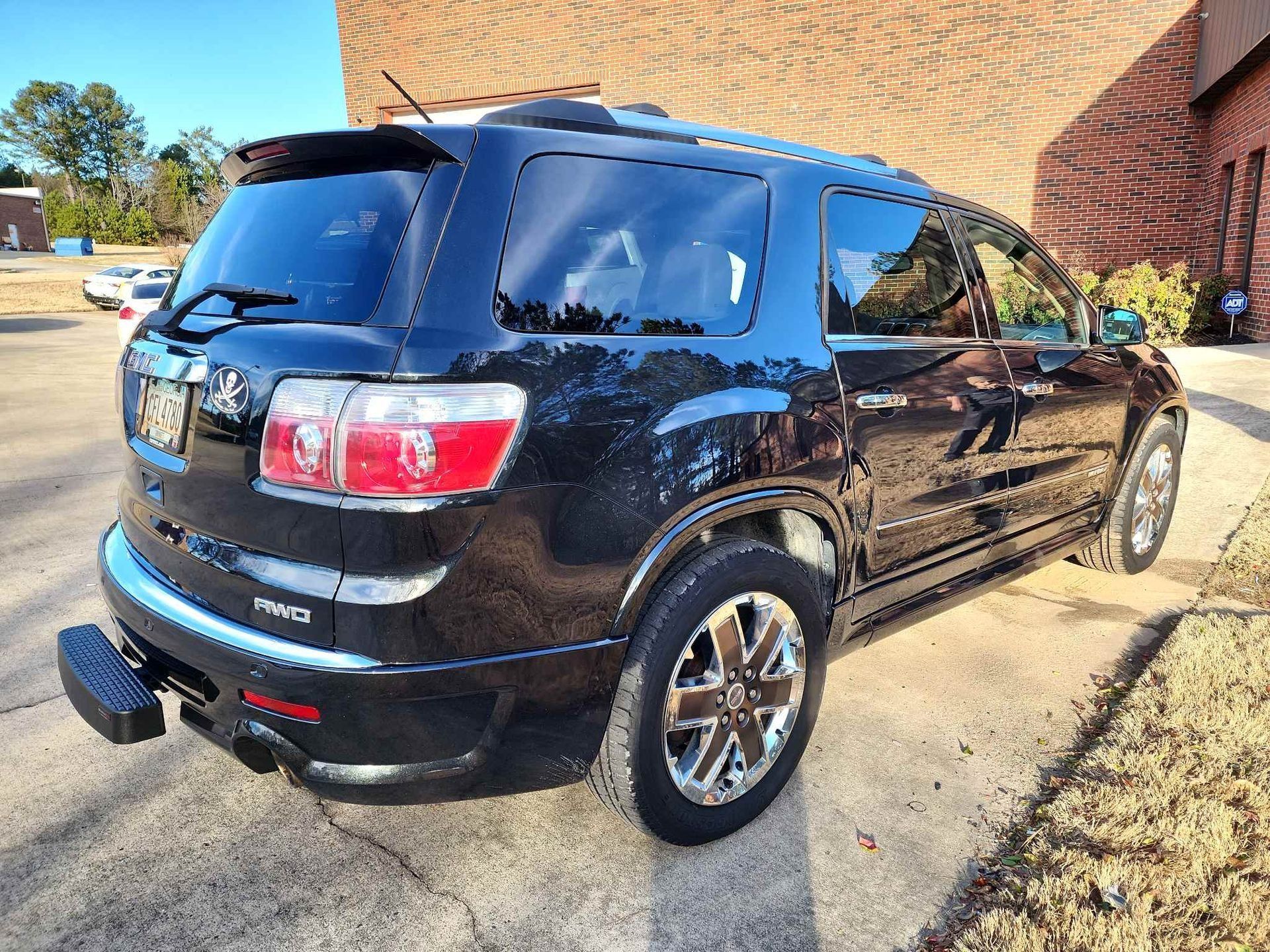 Black GMC SUV parked outside a brick building in daylight, rear three-quarter view.