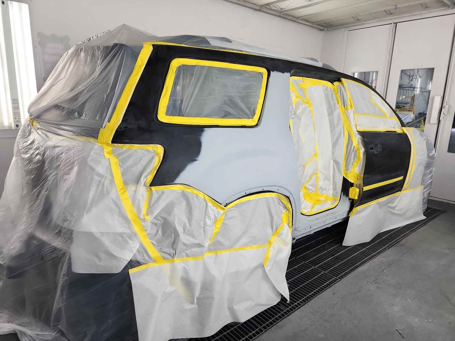 SUV wrapped in plastic and masking tape in a garage, prepared for painting