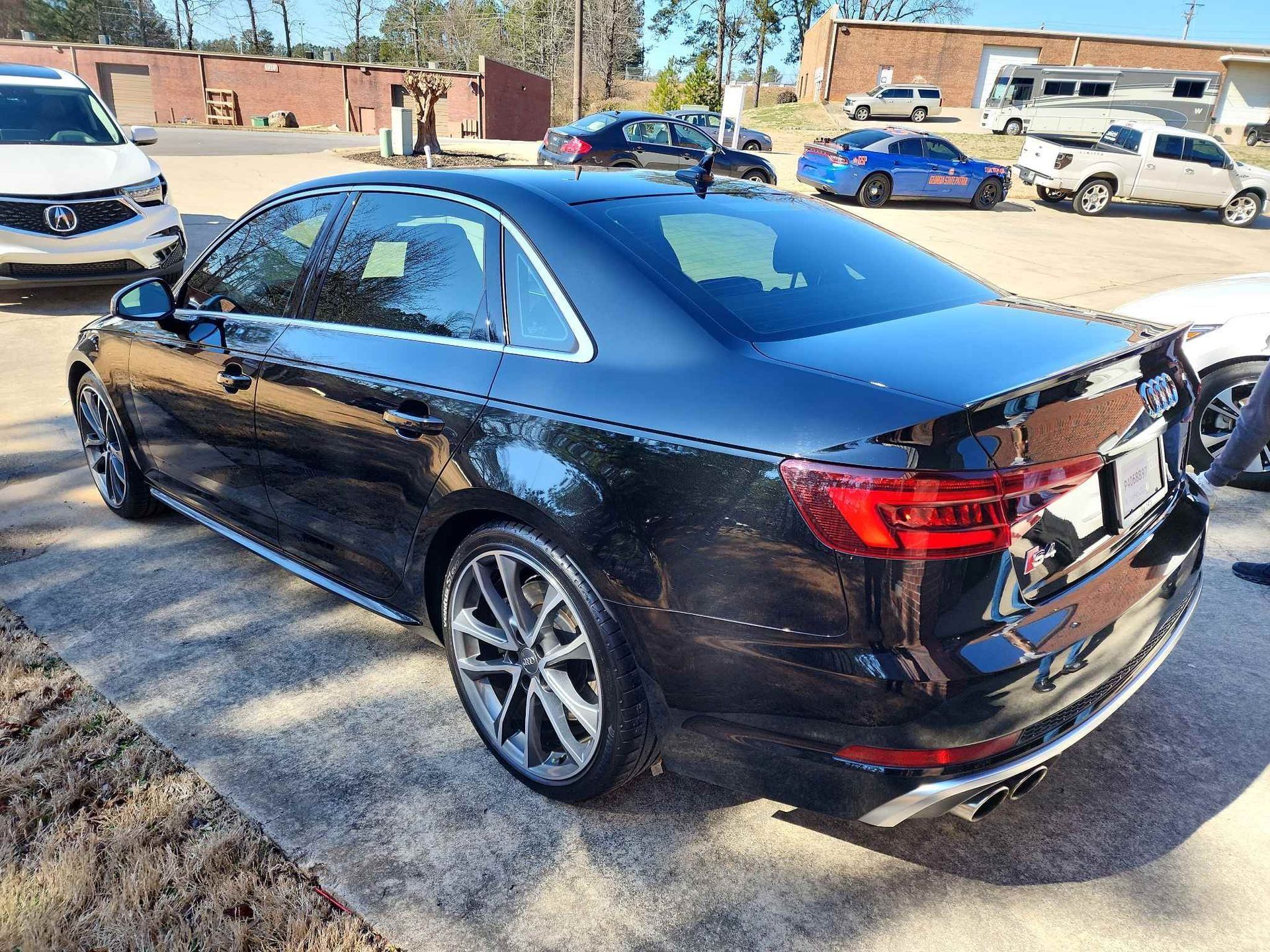 Black sedan parked outdoors in a lot, rear three-quarter view with chrome trim and tinted windows