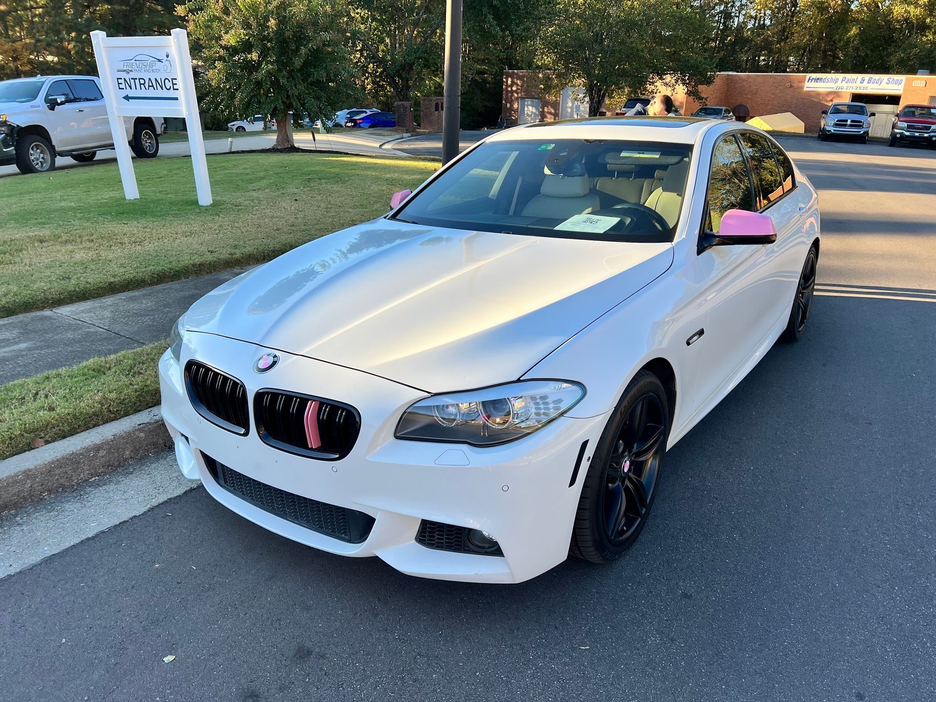 White BMW coupe parked on a street, angled front view with black rims and pink side mirror covers