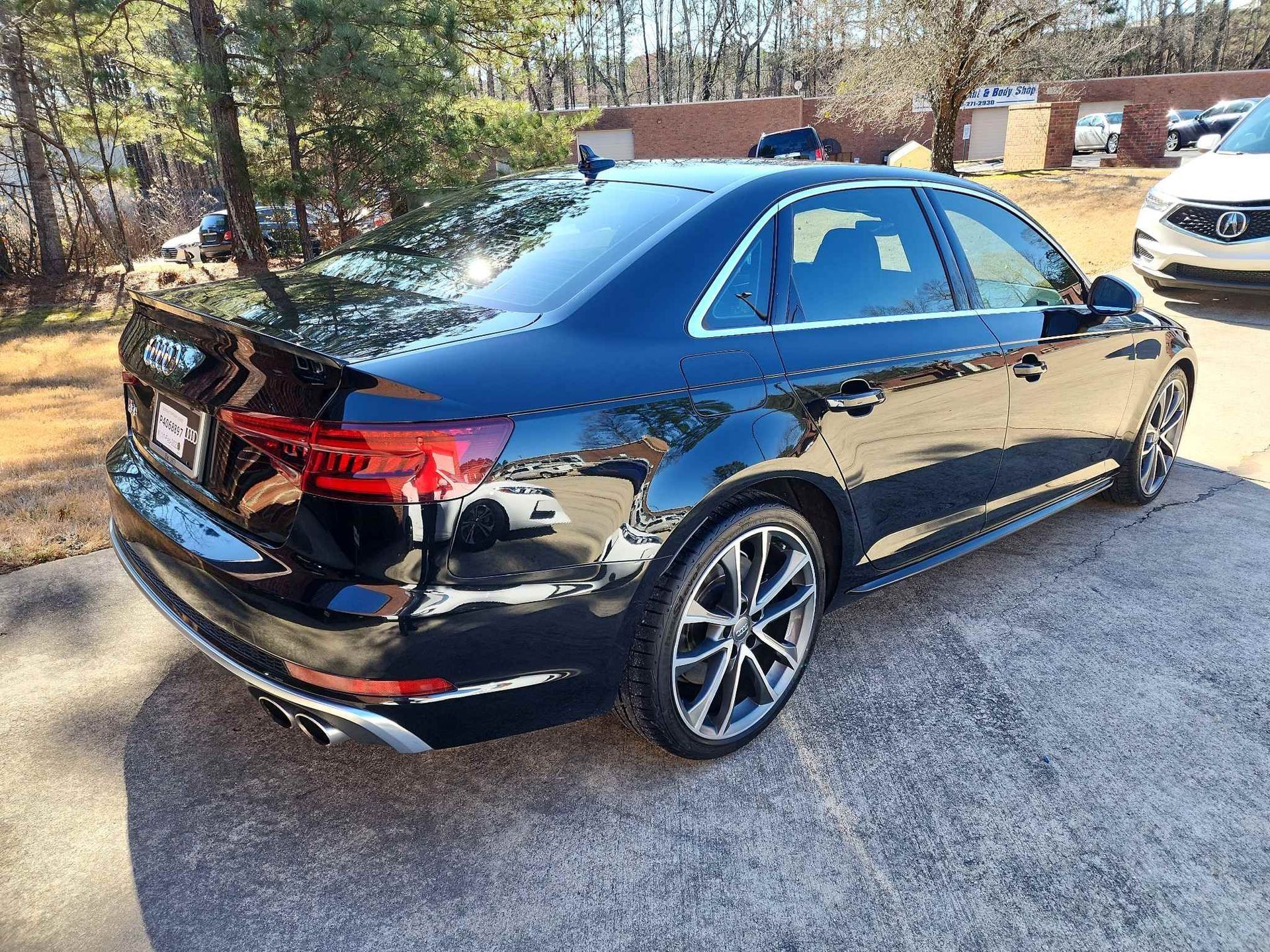 Black Audi sedan parked outdoors on a sunny driveway, rear three-quarter view