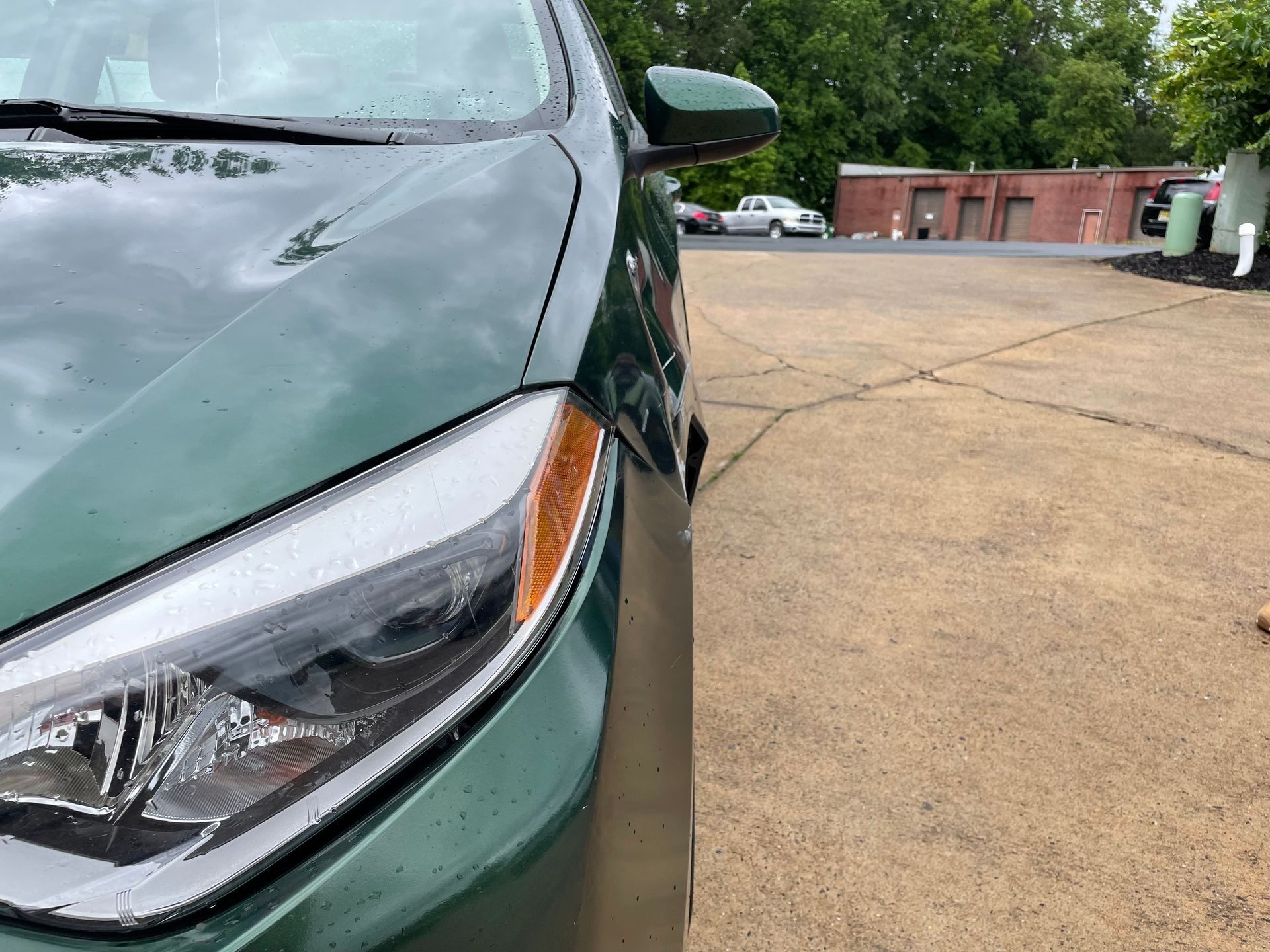 Close-up of a green car’s front headlight beside an empty parking lot and brick building