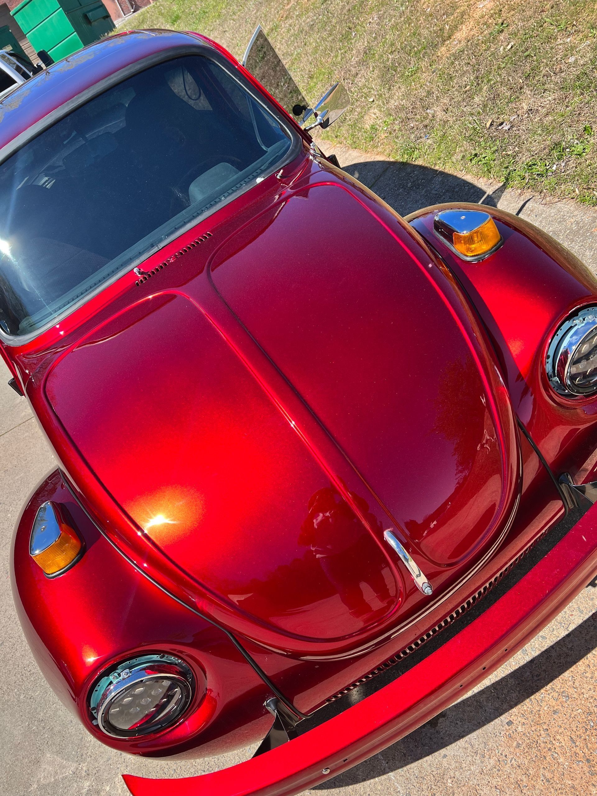 Red Volkswagen Beetle parked on a sunny street, viewed from the front.
