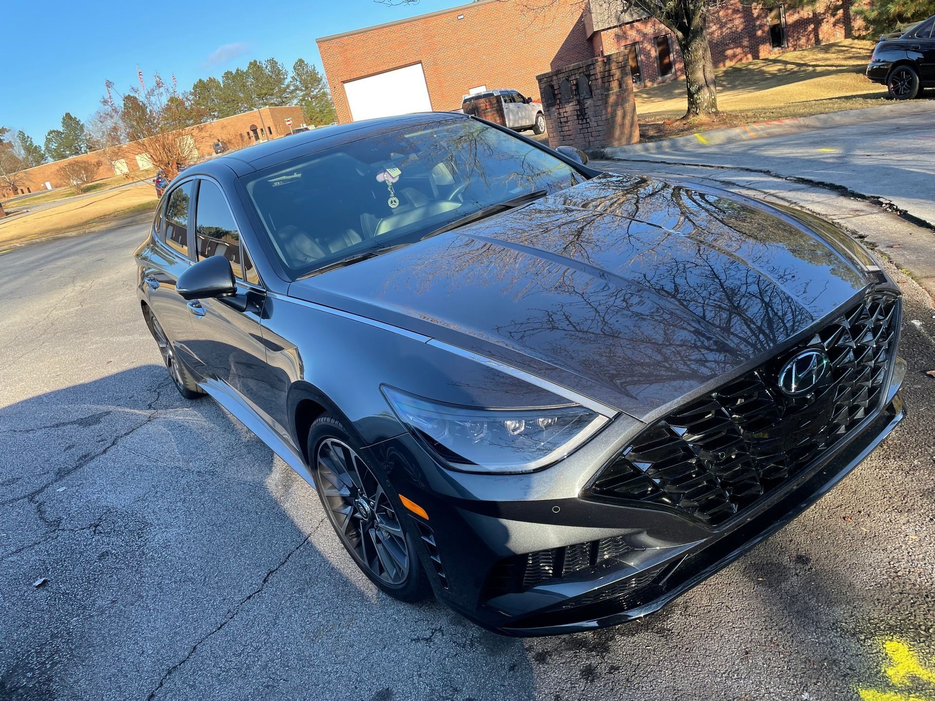 Black sedan parked outdoors on a sunny day, angled front view with a brick building in the background