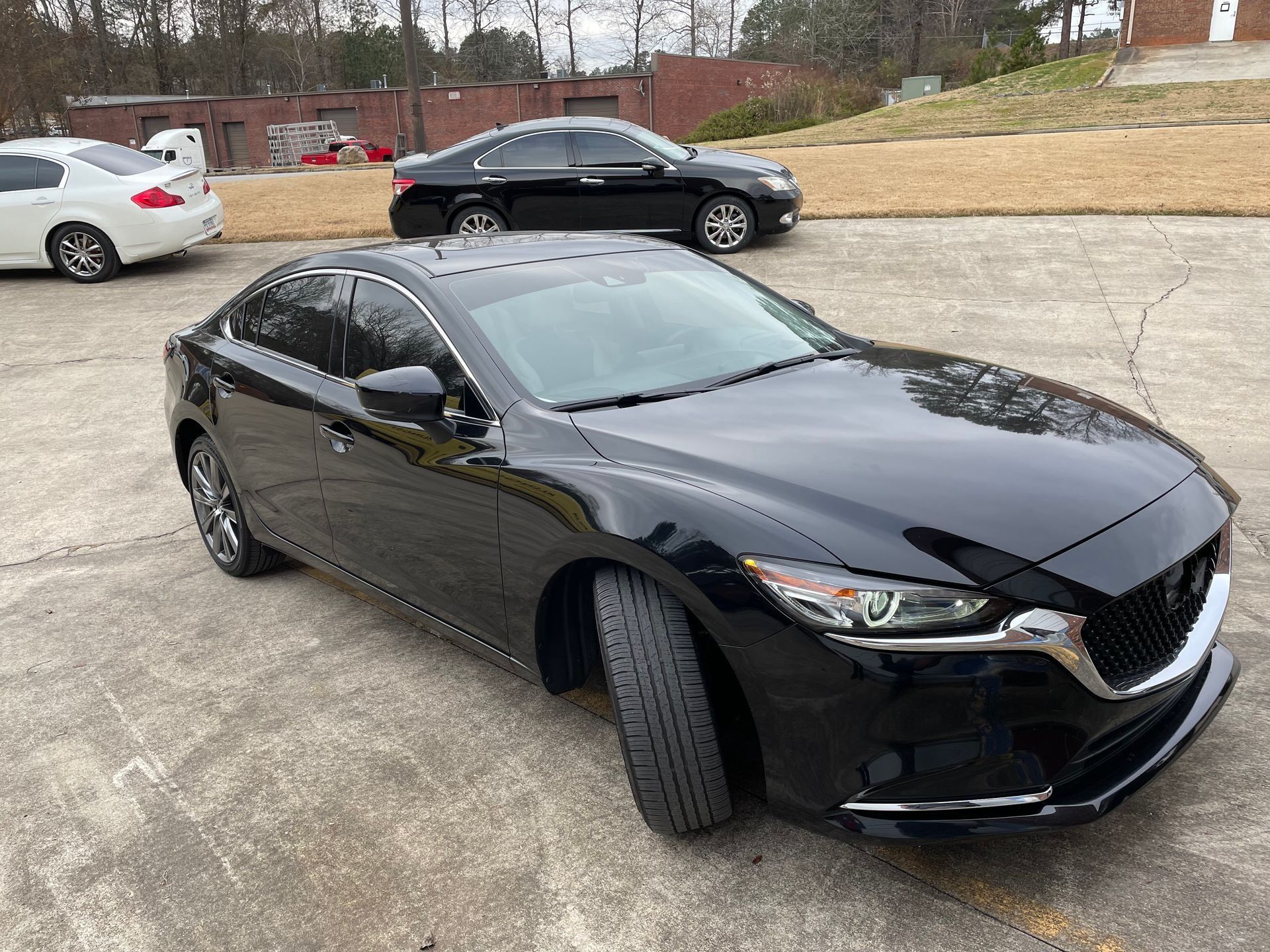 Black sedan parked on a driveway with its front wheels turned, near a white car and another black car.