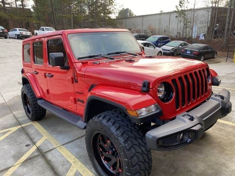 Red Jeep Wrangler parked in a lot, with black off-road tires and a hardtop roof.