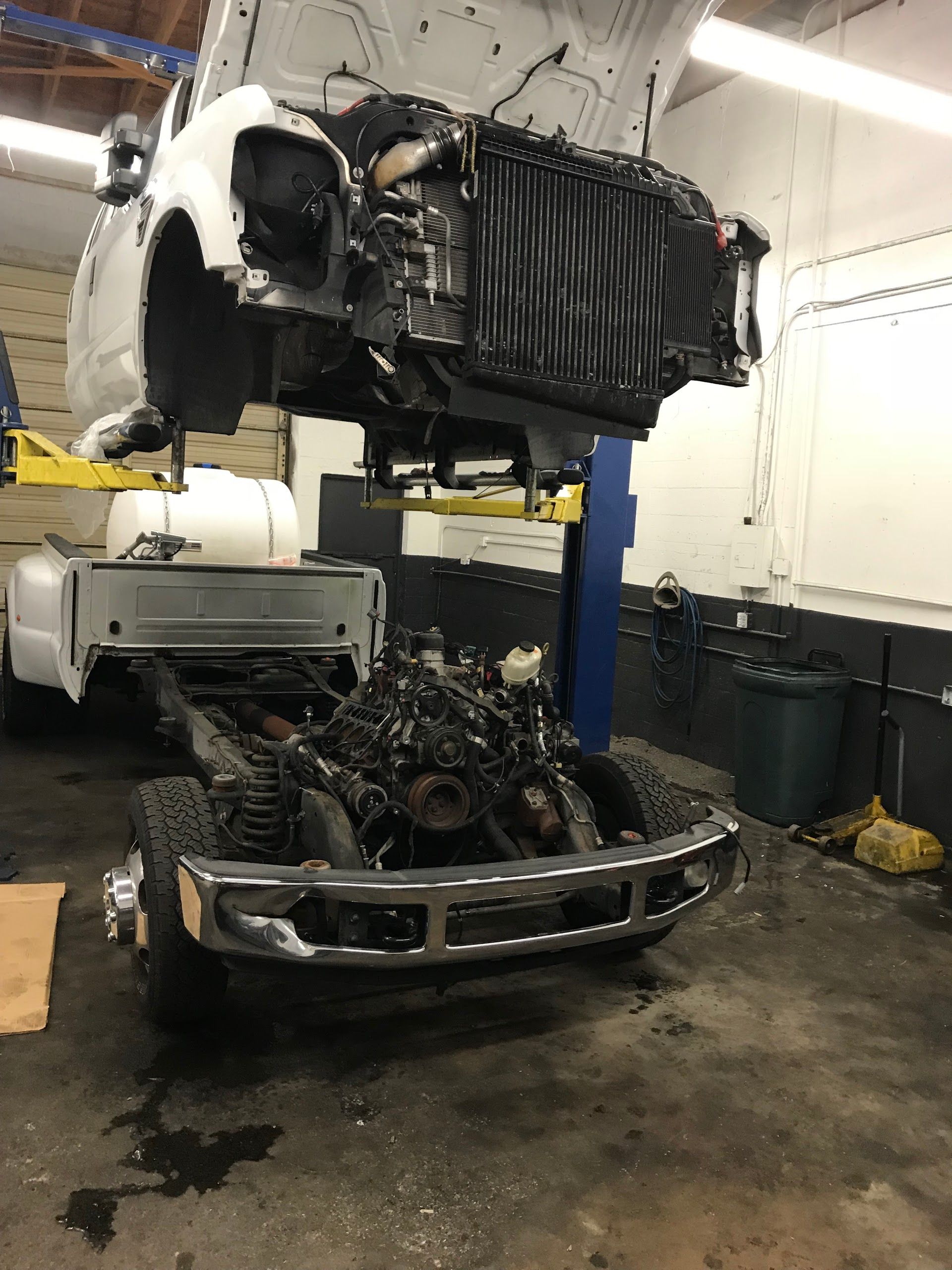 A white truck body is lifted by a shop hoist, exposing the engine, frame, and front bumper of the chassis below. | A-Affordable Auto Repair