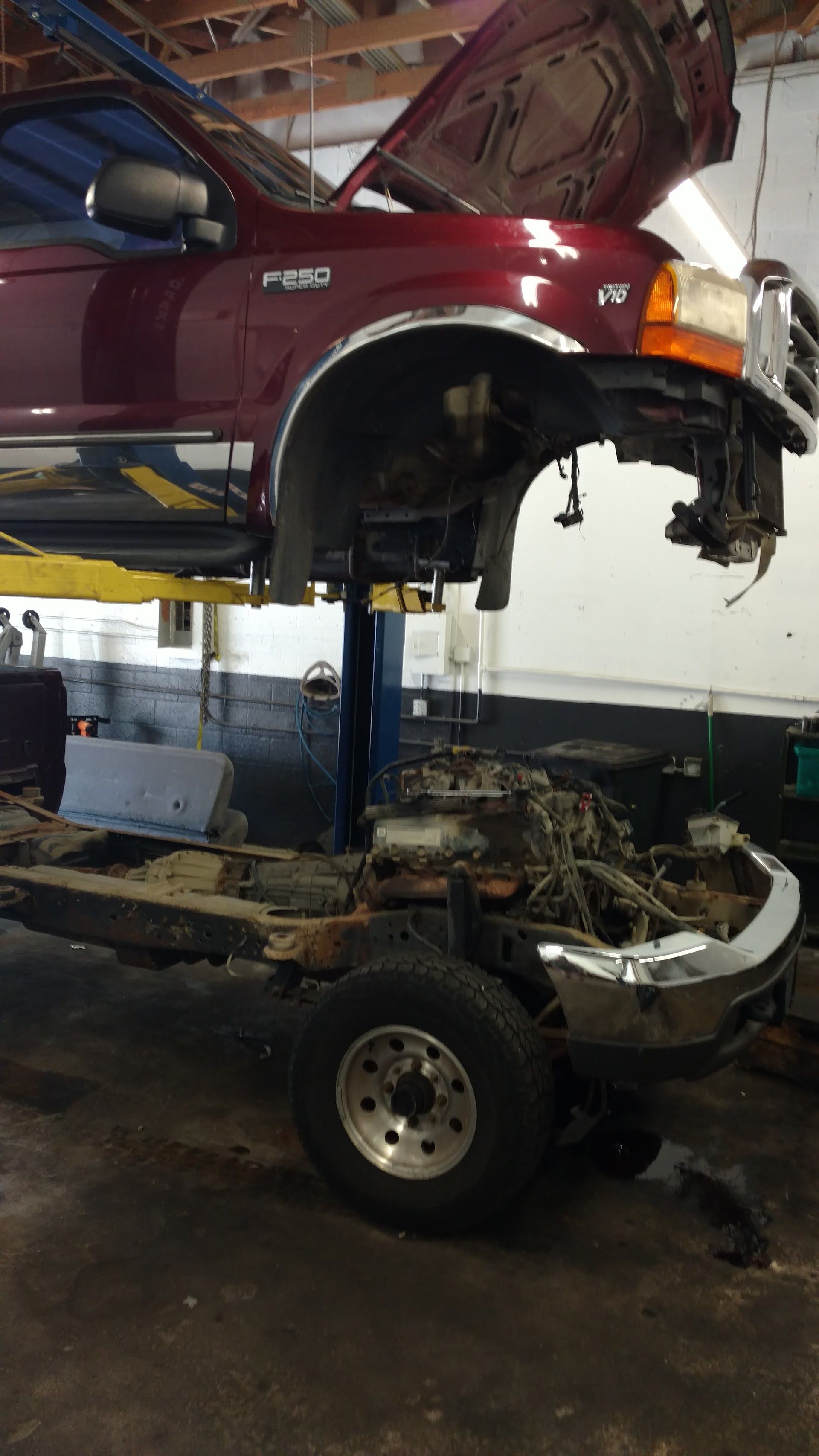 A red Ford F-350 truck body raised on a lift in a garage, separated from its frame and engine on the ground below. | A-Affordable Auto Repair