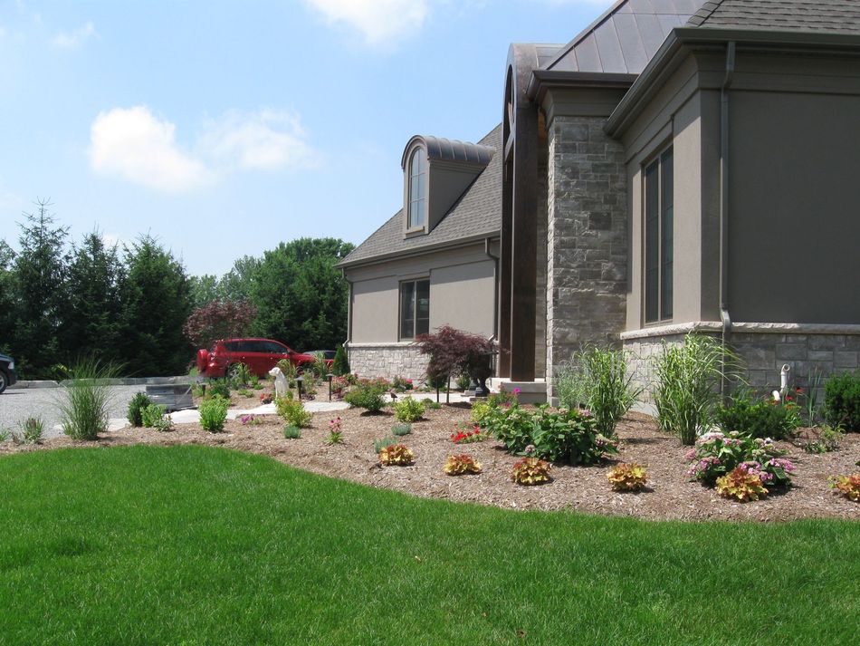 A tan, stone-accented house with a landscaped garden in the front yard under a bright blue sky.