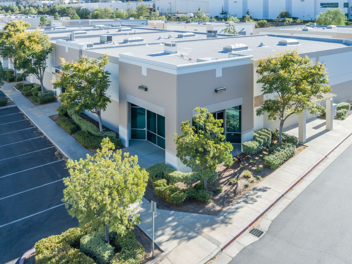 Commercial building exterior with trees, shrubs, parking lot, and sidewalk.
