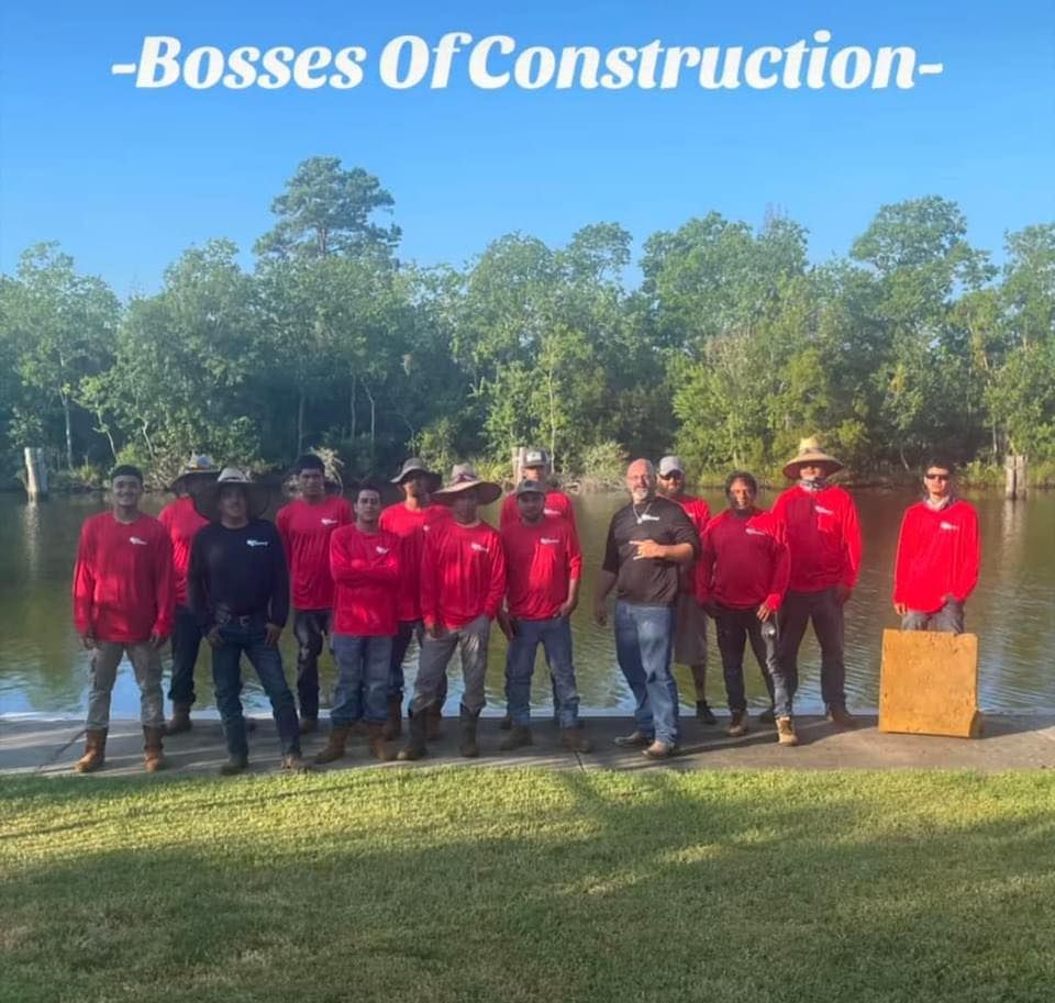A group of construction workers are posing for a picture in front of a body of water.
