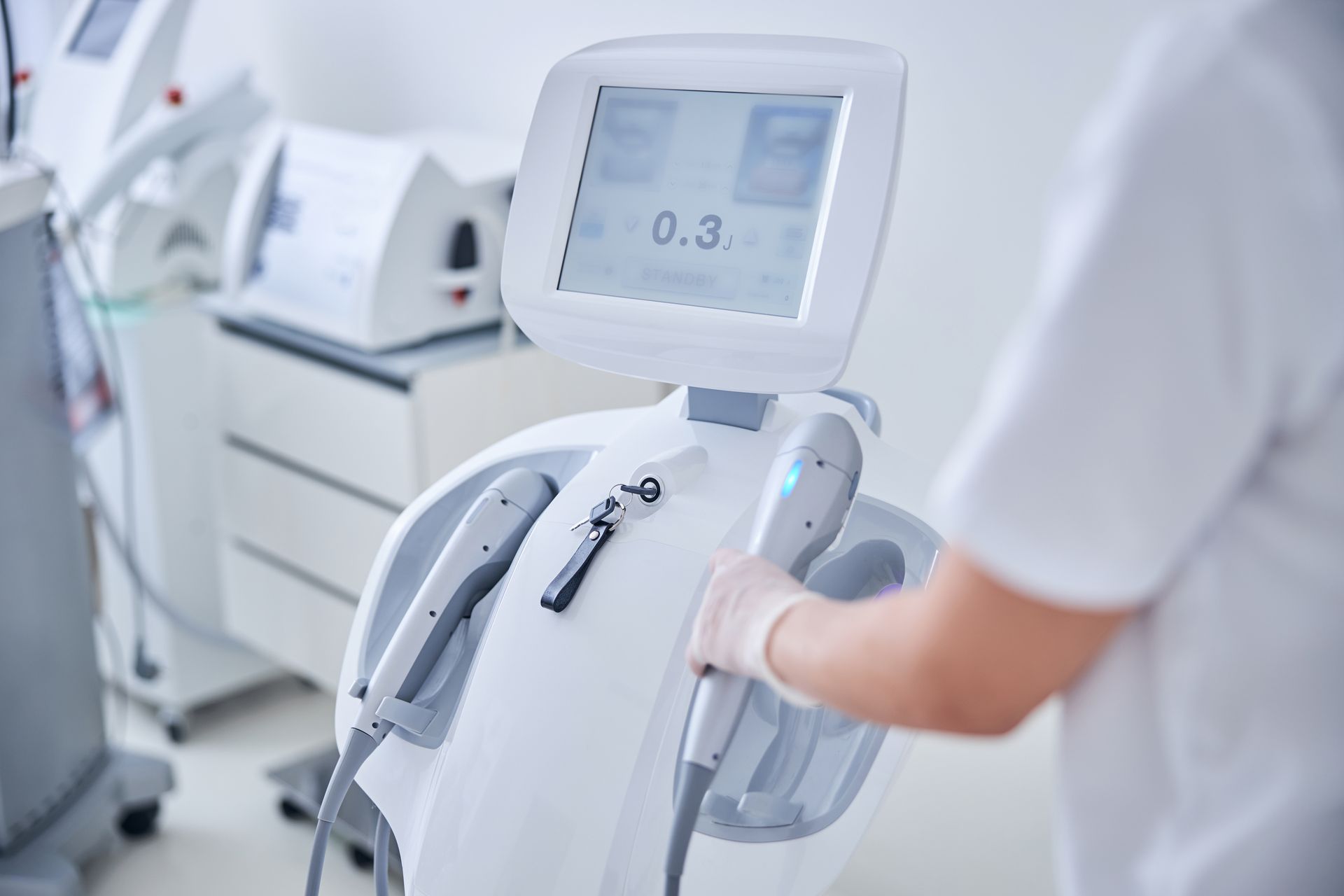 Healthcare worker operating a white medical device with touchscreen in a clinical setting