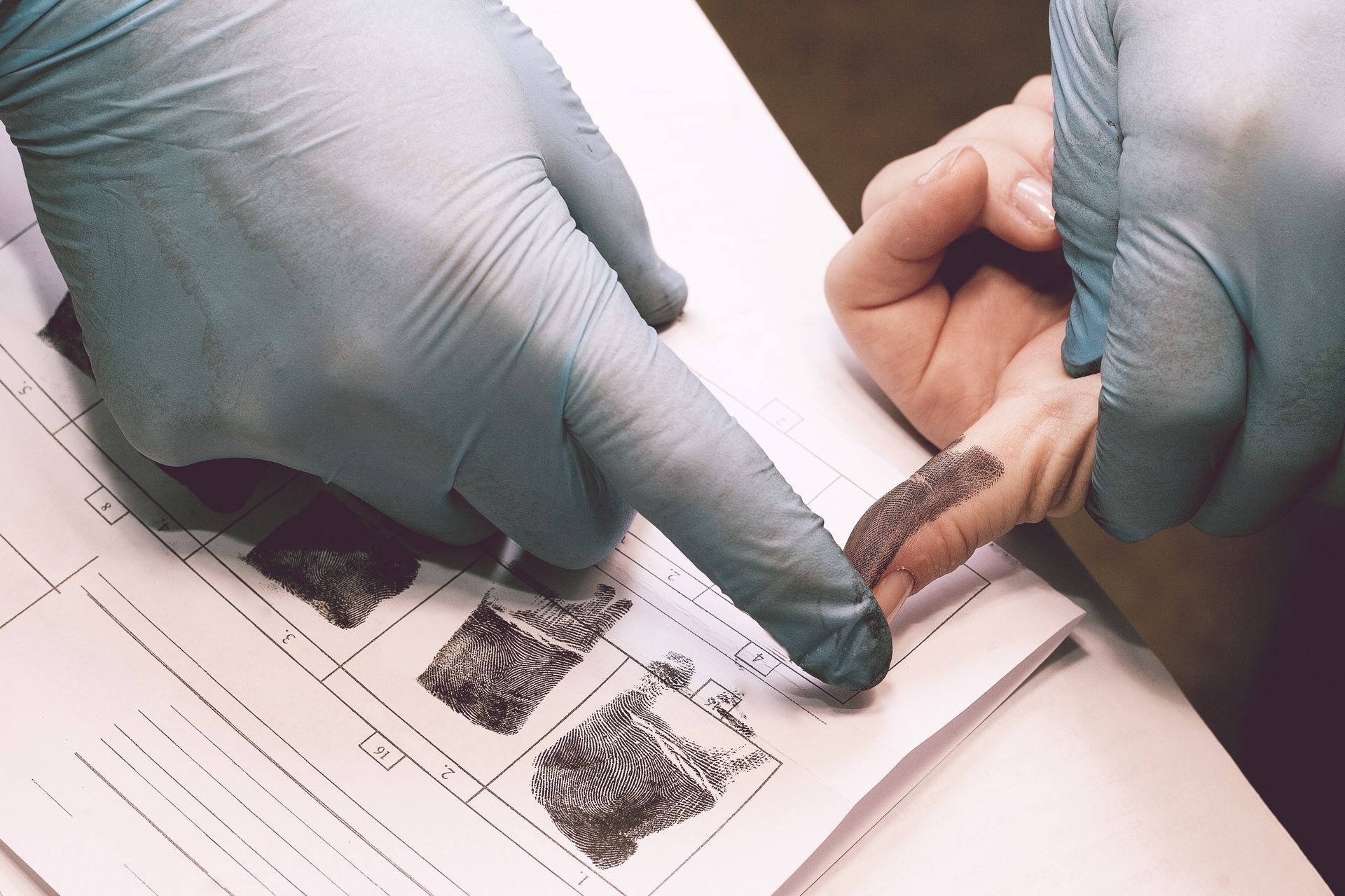 Gloved hands examining a fingerprint card with a magnifying tool on a desk