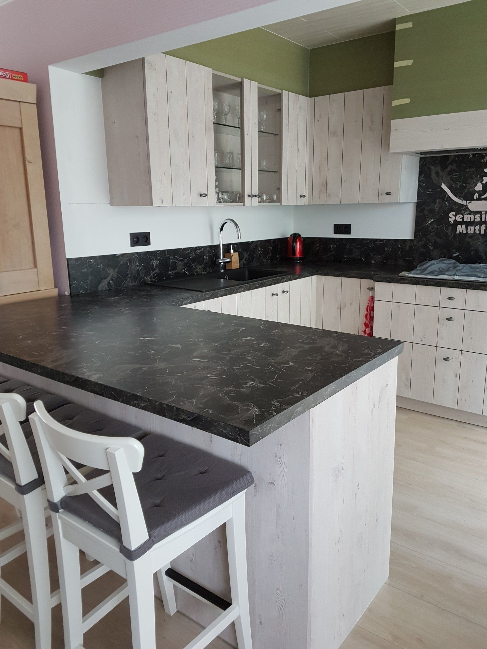 U-vormige keuken met lichte houten kasten, donkere aanrechtbladen en een ontbijtbar met witte krukken.